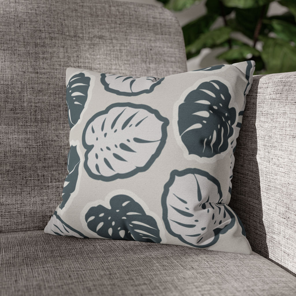 Einzelne Ansicht des Kissens auf einem grauen Sofa mit einer Monstera Pflanze im Hintergrund. 