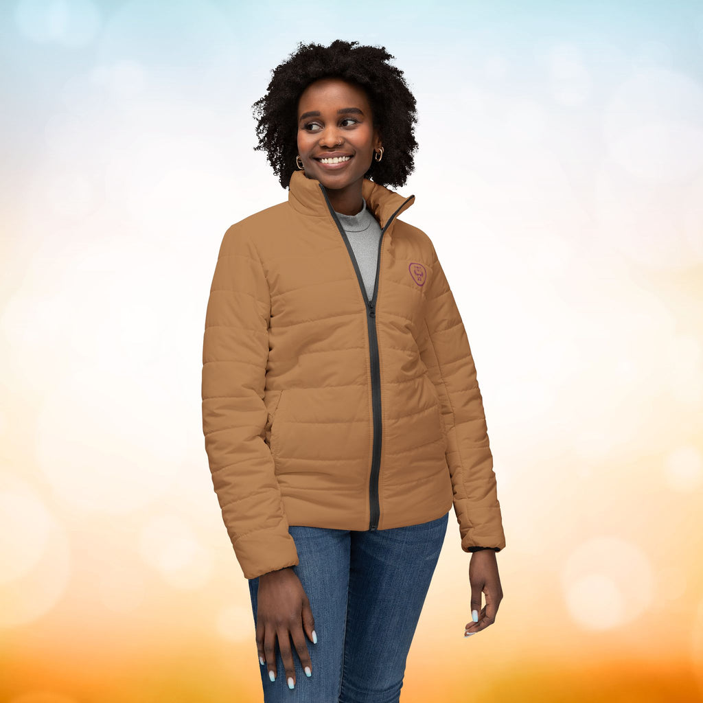 Ein weibliches Model zeigt die Damen-Pufferjacke in der Vorderansicht in einem Persian-Orange farbton. Die Jacke ist horizontal gesteppt, hat eine glatte Oberfläche, einen hohen Stehkragen und einen durchgehenden Reißverschluss. Designed, by Just a Girl.

