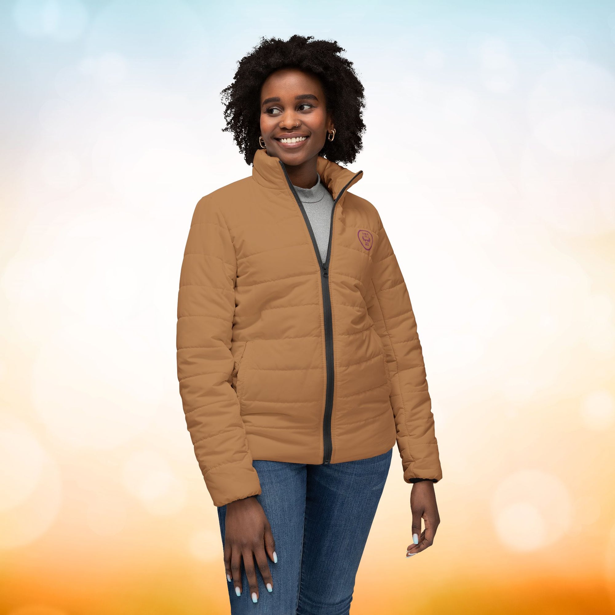 Ein weibliches Model zeigt die Damen-Pufferjacke in der Vorderansicht in einem Persian-Orange farbton. Die Jacke ist horizontal gesteppt, hat eine glatte Oberfläche, einen hohen Stehkragen und einen durchgehenden Reißverschluss. Designed, by Just a Girl.

