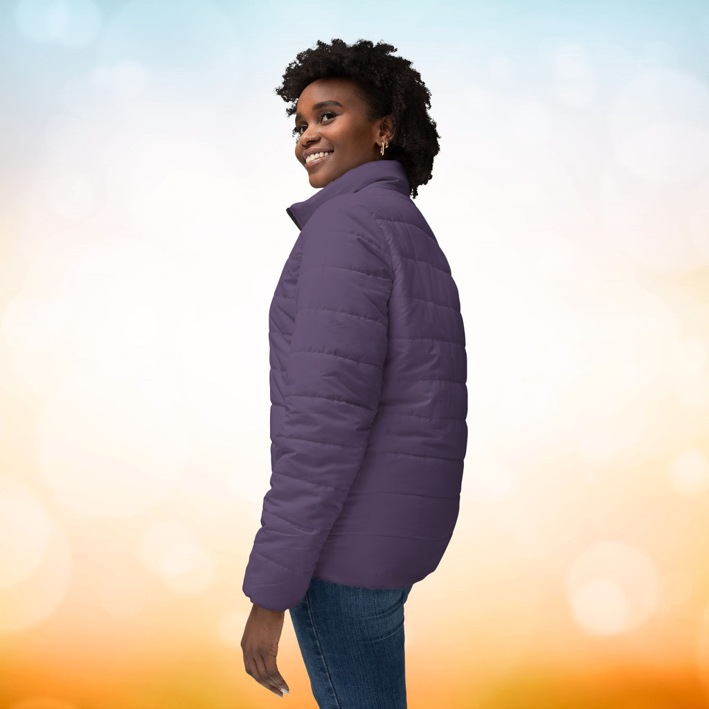 Das weibliche Model trägt eine  Damen-Pufferjacke in einem dunklem Dusty Plum Farbton. Die Jacke ist horizontal gesteppt, hat eine glatte Oberfläche, einen hohen Stehkragen sie präsentiert die Jacke von der linken Seite. Designed, by Just a Girl.