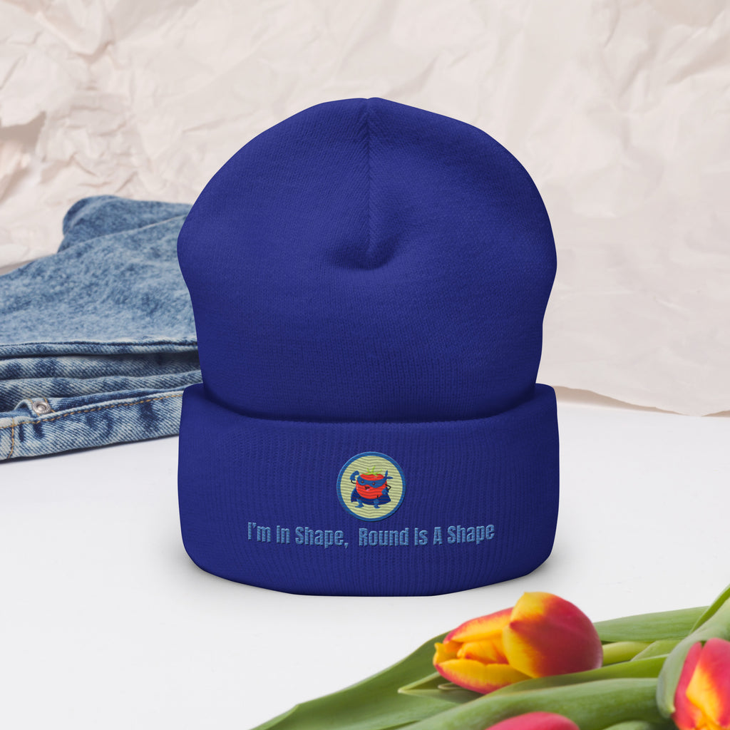 Ein Royal Blaues Cuffed Beanie mit einem aufgesticktem Patch eines Tomaten Superhleden (Cartoon) in einem Runden blau-salbeigrünem Rahmen sowie einen schlichten Schriftzug darunter der lautet: "I´m in Shape, Round is A Shape!" auf der Vorderseite. Dekoriert mit Jeans und Blumen.  Designed, by Just a Girl.