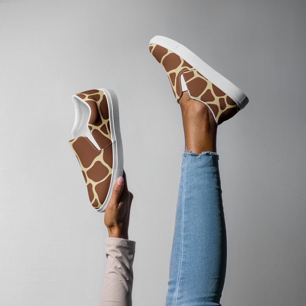 Ein weibliches Model zeigt tragend ein Bein in die Luft gestreckt und mit der anderen Hand den 2. Schuh zeigend mit einem Giraffenmuster in Brauntönen und Creme auf einem hellen Hintergrund. Designed, by Just a Girl.