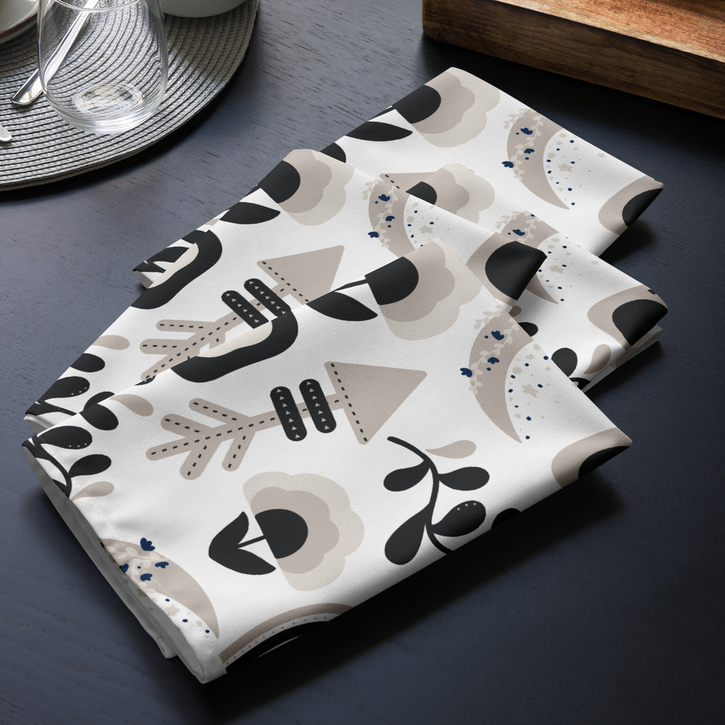 4er Set Stoff Servietten gefaltet auf dem Tisch platziert. Das Muster zeigt ein abstraktes Design mit Boho-Elementen wie stilisierten Pfeilen, einem Regenbogen, einer gepunkteten Mondsichel und floralen Motiven in Schwarz, Beige und Brauntönen.