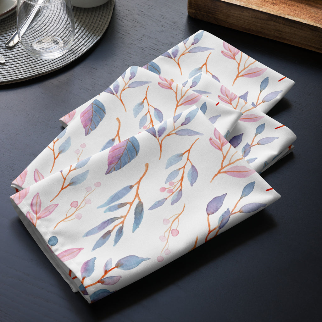 4er Set Stoff Servietten gefaltet auf dem Tisch platziert. Der Hintergrund der Servietten ist weiß und zeigt ein filigranes Muster aus Zweigen mit Blättern und kleinen Beeren. Die Blätter sind in zarten Blau-, Lila- und Rosatönen gehalten, während die Beeren dunkelblau sind.