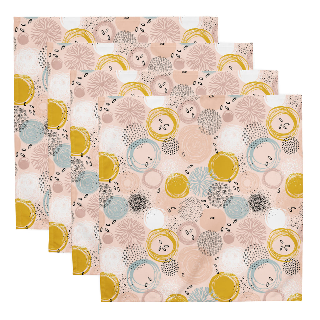 Ein Set aus vier Stoff-Servietten, freigestellt auf weißem Hintergrund. Die Servietten haben einen rosafarbenen Hintergrund und zeigen ein abstraktes Muster aus Kreisen in Gelb, Blau und Weiß sowie kleine schwarze Sprenkel.