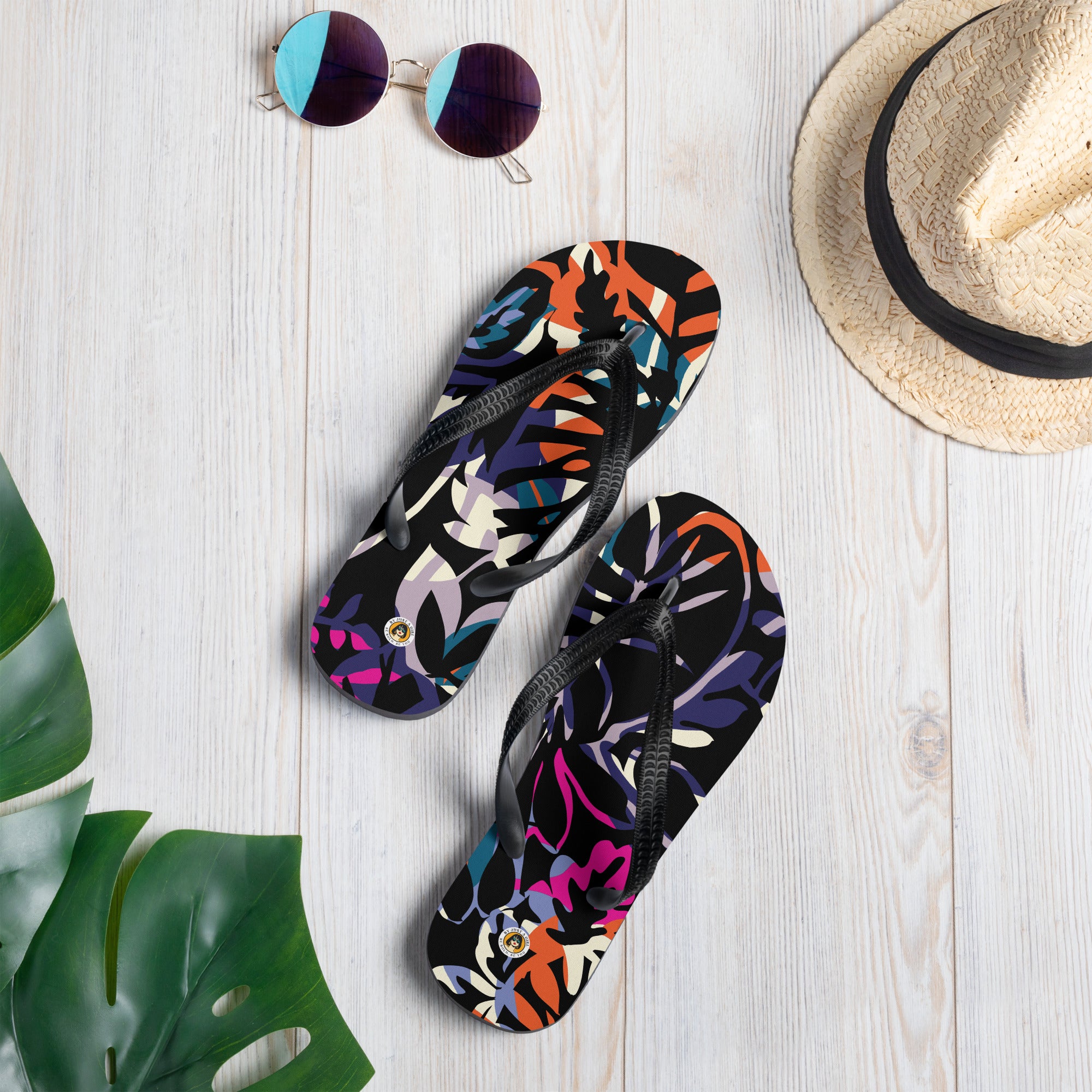 Ein Paar schwarze Herren-Flip-Flops mit einem Obermaterial, das ein dichtes, abstraktes Dschungel- oder Blättermuster auf schwarzem Grund zeigt. Das Muster ist in leuchtenden Neonfarben wie Orange, Pink, Blau, Lila und Hellgrün gehalten, die sich überlappen und einen dynamischen Effekt erzeugen. Die Riemen sind schwarz und haben eine strukturierte Oberfläche.