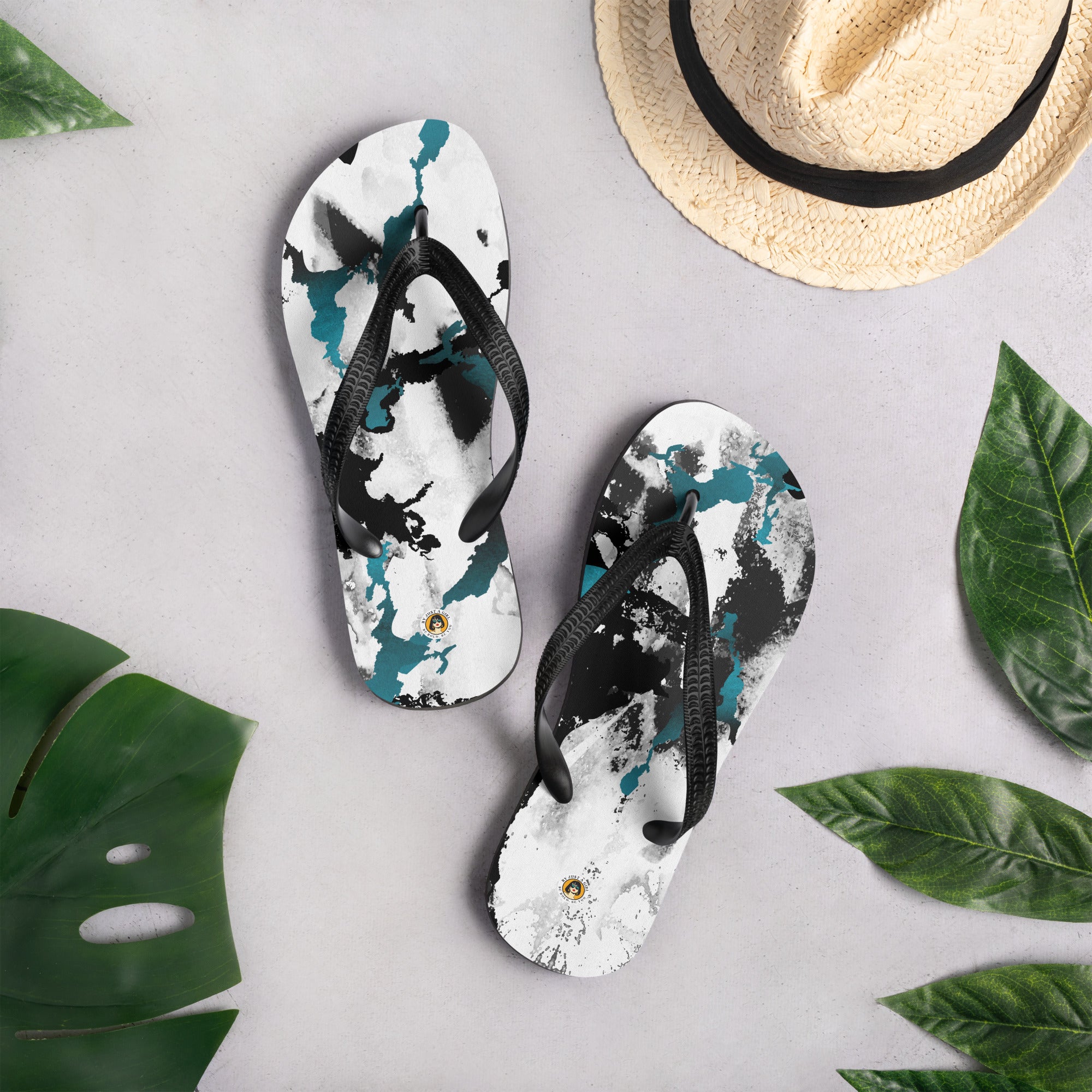 Ein Paar schwarze Herren-Flip-Flops mit einem Obermaterial, das ein abstraktes, dynamisches Muster aus unregelmäßigen schwarzen, weißen und türkisen Farbflächen oder Spritzern auf einem hellen Hintergrund zeigt. Die Riemen sind schwarz und haben eine strukturierte Oberfläche.