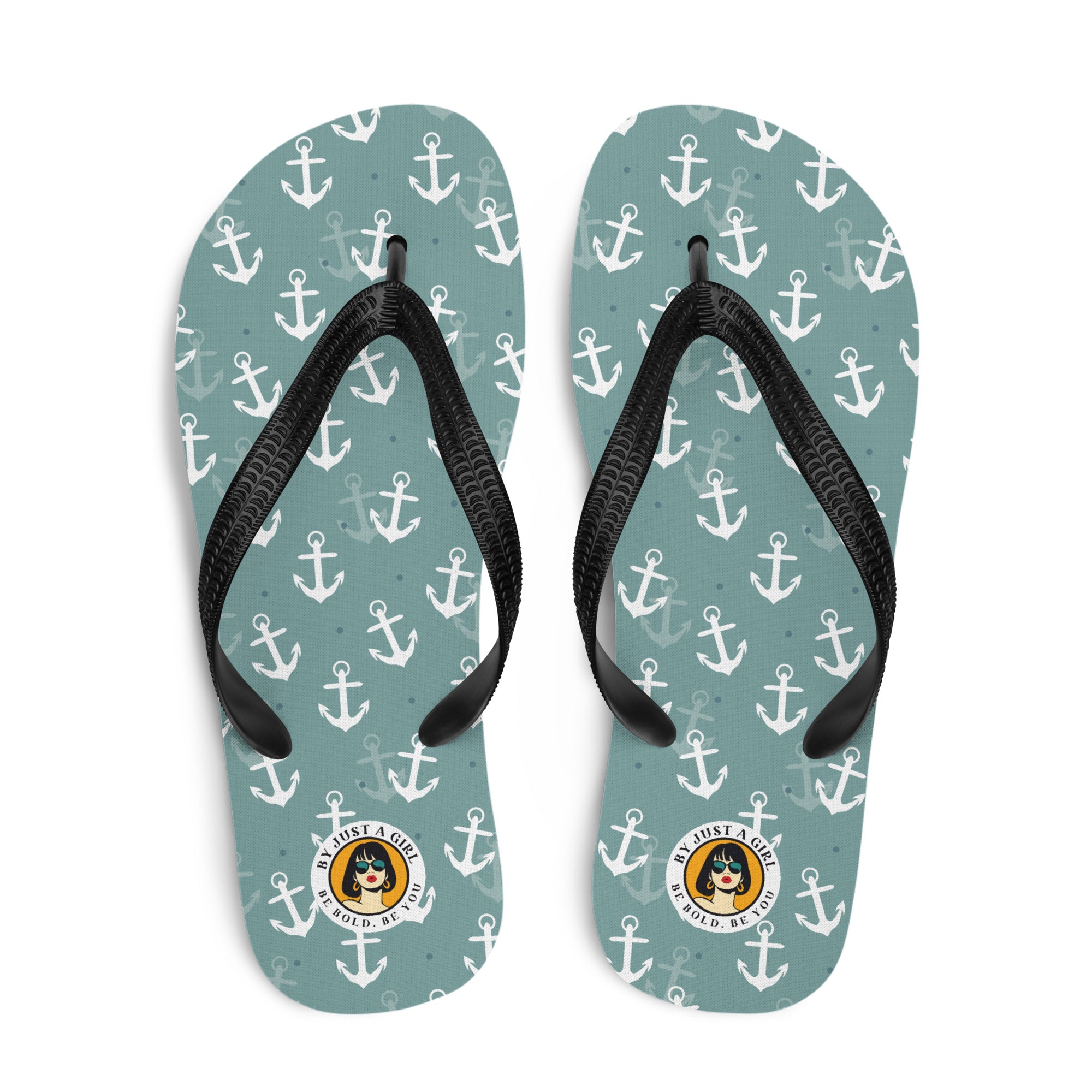Ein Paar Flip-Flops mit einem Obermaterial in einem gedämpften Türkis- oder Blaugrünton, das mit einem wiederkehrenden Muster aus stilisierten weißen Ankern und kleinen grauen Punkten bedeckt ist. Die Riemen sind schwarz und haben eine strukturierte Oberfläche. Auf der Ferse jedes Flip-Flops befindet sich ein rundes gelbes Emblem mit dem Text "BY JUST A GIRL" und "BE BOLD. BE YOU" sowie dem stilisierten Kopf einer Frau mit Bob-Frisur und Sonnenbrille.