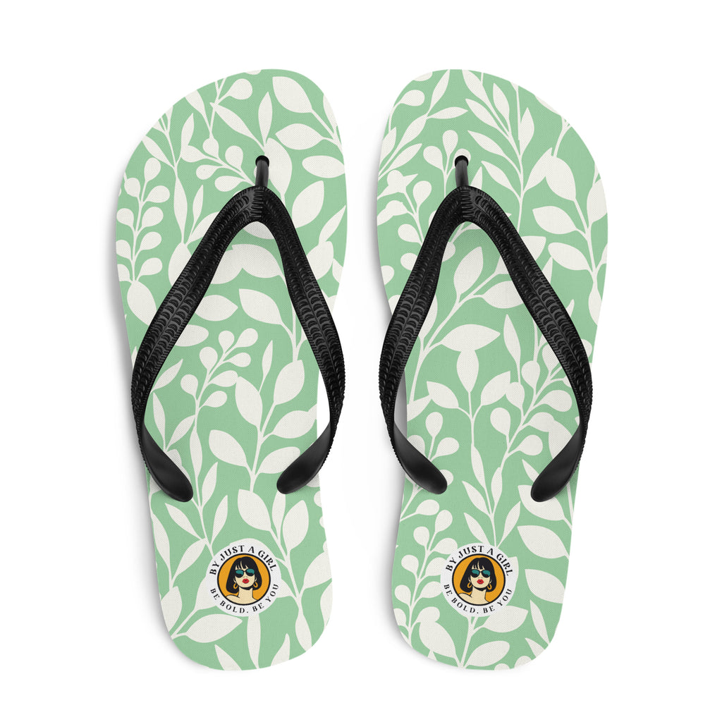 Ein Paar Flip-Flops mit einem hellmintgrünen Untergrund, der mit einem wiederkehrenden Muster aus stilisierten weißen Blättern und kleinen runden Beeren bedeckt ist. Die Riemen sind schwarz und haben eine strukturierte Oberfläche. Auf der Ferse jedes Flip-Flops befindet sich ein rundes gelbes Emblem mit dem Text "BY JUST A GIRL" und "BE BOLD. BE YOU" sowie dem stilisierten Kopf einer Frau mit Bob-Frisur und Sonnenbrille.