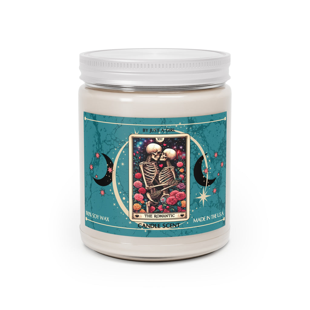 Eine weiße Kerze in einem durchsichtigen Glasgefäß mit weißem Deckel. Das Etikett ist türkisfarben mit Mond- und Sternmotiven und zeigt in der Mitte eine goldgerahmte Tarotkarte mit zwei sich umarmenden Skeletten, umgeben von roten und rosafarbenen Rosen. Der Text auf dem Etikett lautet "BY JUST A GIRL"