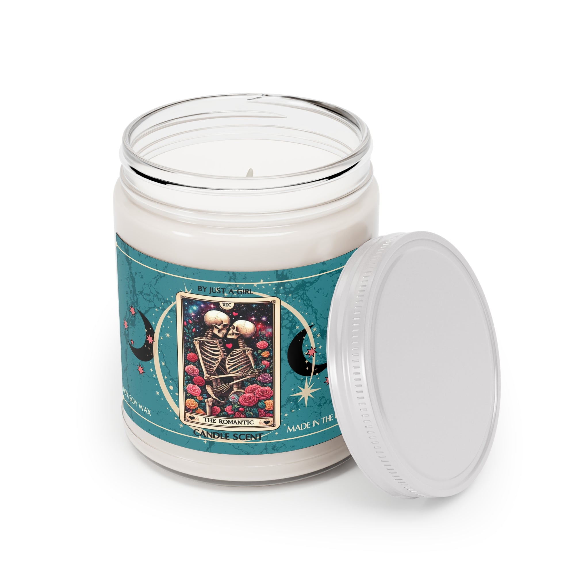Eine weiße Kerze in einem durchsichtigen Glasgefäß mit weißem Deckel. Das Etikett ist türkisfarben mit Mond- und Sternmotiven und zeigt in der Mitte eine goldgerahmte Tarotkarte mit zwei sich umarmenden Skeletten, umgeben von roten und rosafarbenen Rosen. Der Text auf dem Etikett lautet "BY JUST A GIRL"