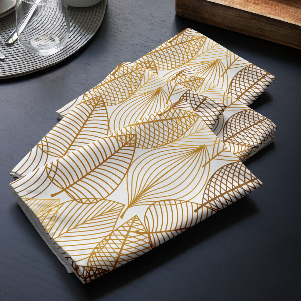 4er Set gefaltete Golden Leaves Servietten präsentiert auf dem Tisch liegend. Das Muster zeigt stilisierte Blätter in verschiedenen Gold- und Brauntönen. Einige Blätter sind nur durch feine Linien gezeichnet, andere sind mit einem gekreuzten Muster gefüllt. 