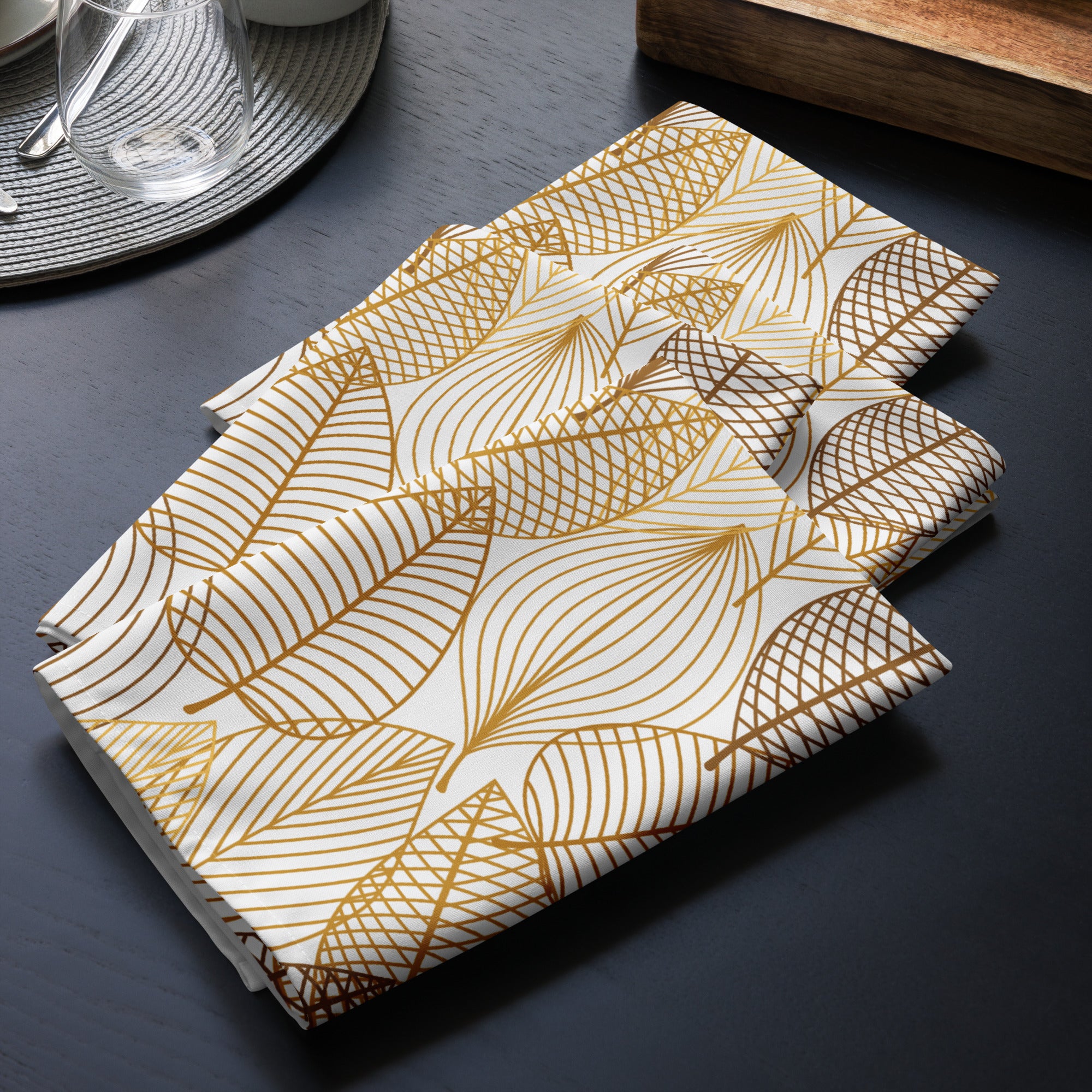 4er Set gefaltete Golden Leaves Servietten präsentiert auf dem Tisch liegend. Das Muster zeigt stilisierte Blätter in verschiedenen Gold- und Brauntönen. Einige Blätter sind nur durch feine Linien gezeichnet, andere sind mit einem gekreuzten Muster gefüllt. 