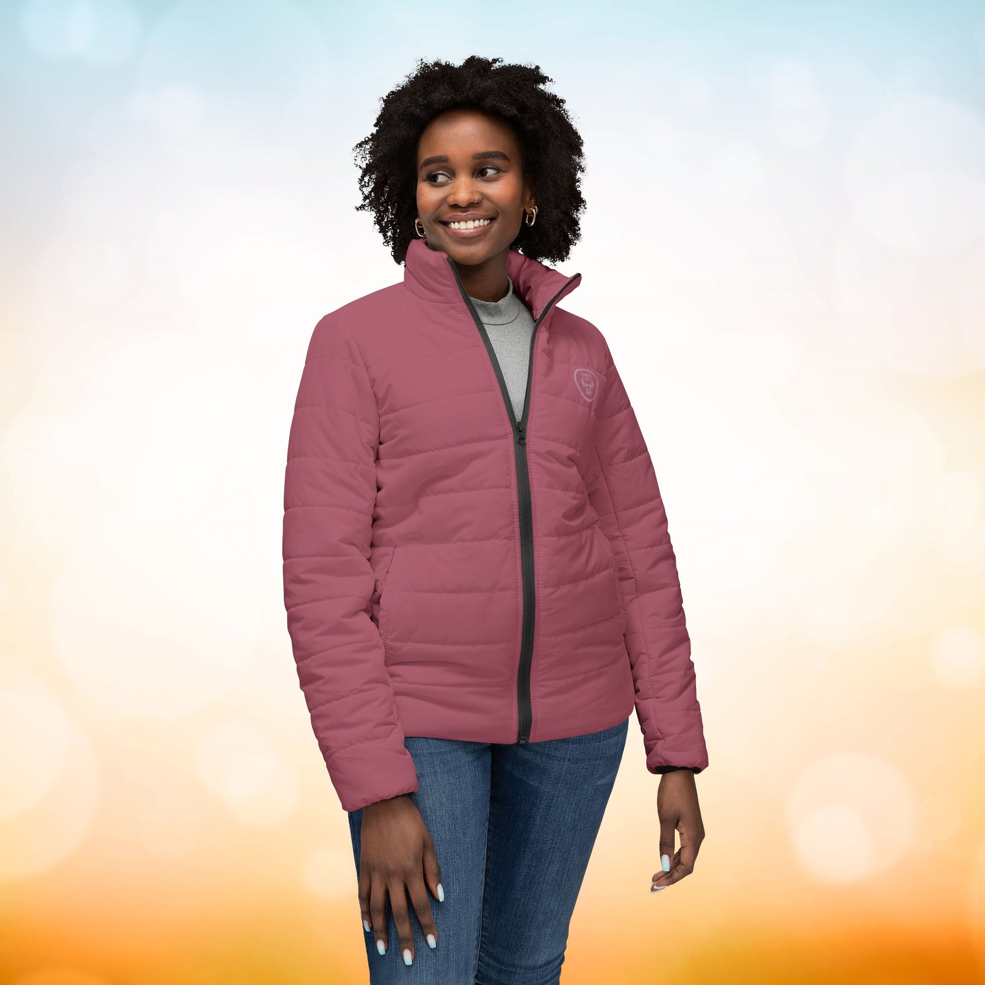 Ein weibliches Model trägt die  Damen-Pufferjacke in einem zarten Rosenstaub. Die Jacke ist horizontal gesteppt, hat eine glatte Oberfläche, einen hohen Stehkragen und einen durchgehenden Reißverschluss. Designed, by Just a Girl.