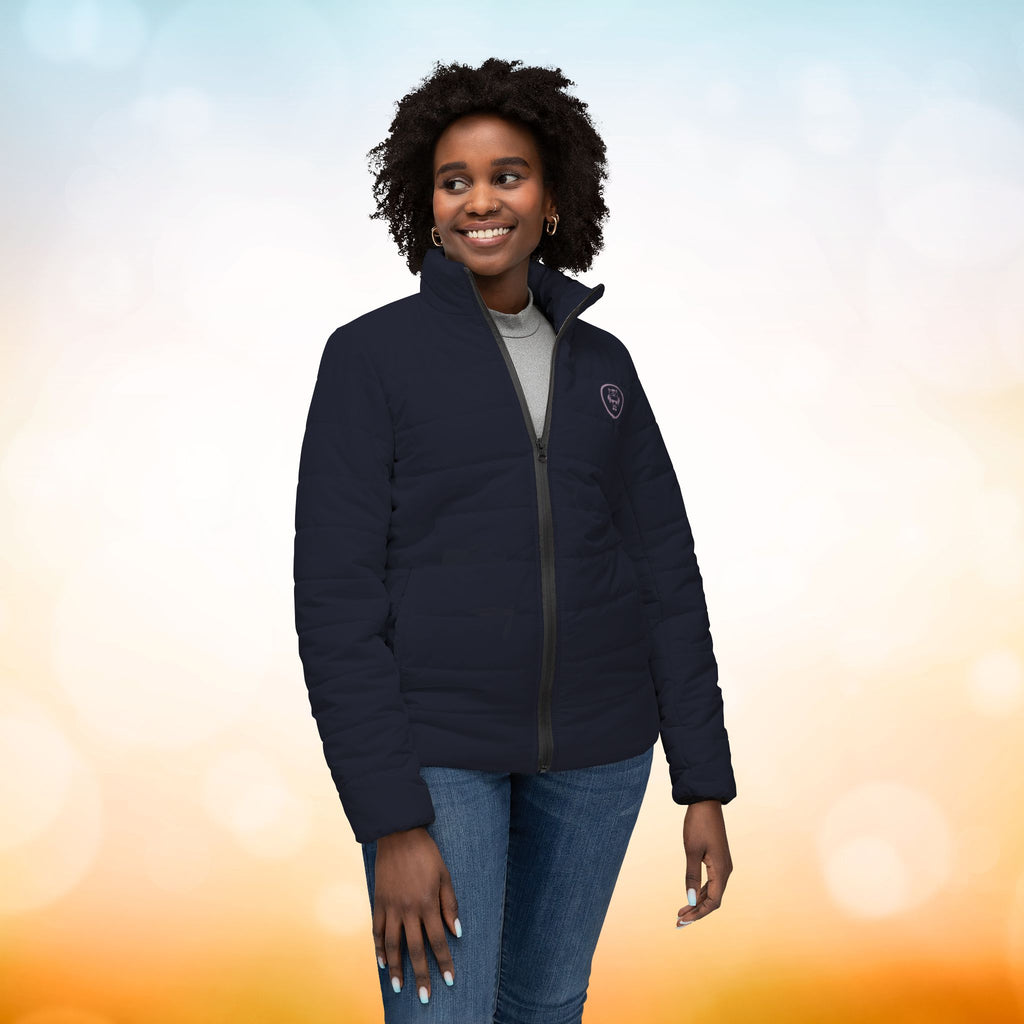 Ein weibliches Model trägt eine  Damen-Pufferjacke in Black Pearl Ansicht von vorne. Die Jacke ist horizontal gesteppt, hat eine glatte Oberfläche, einen hohen Stehkragen und einen durchgehenden Reißverschluss. Designed, by Just a Girl