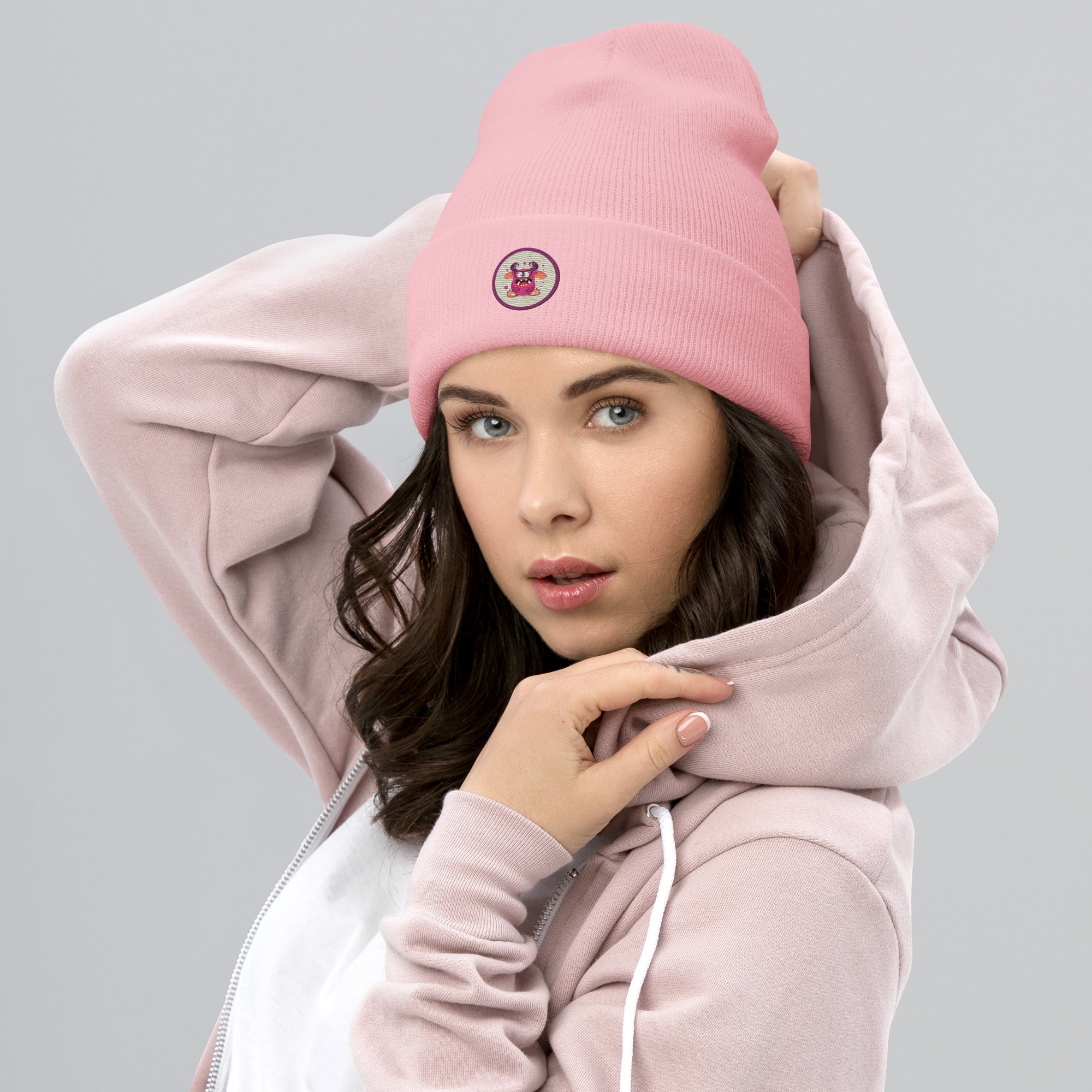 weibliches Model trägt baby pinke Cuffed Beanie mit aufgesticktem, pinkem Monster-Gesicht in einem runden lila Rahmen auf der Vorderseite. Designed, by Just a Girl.