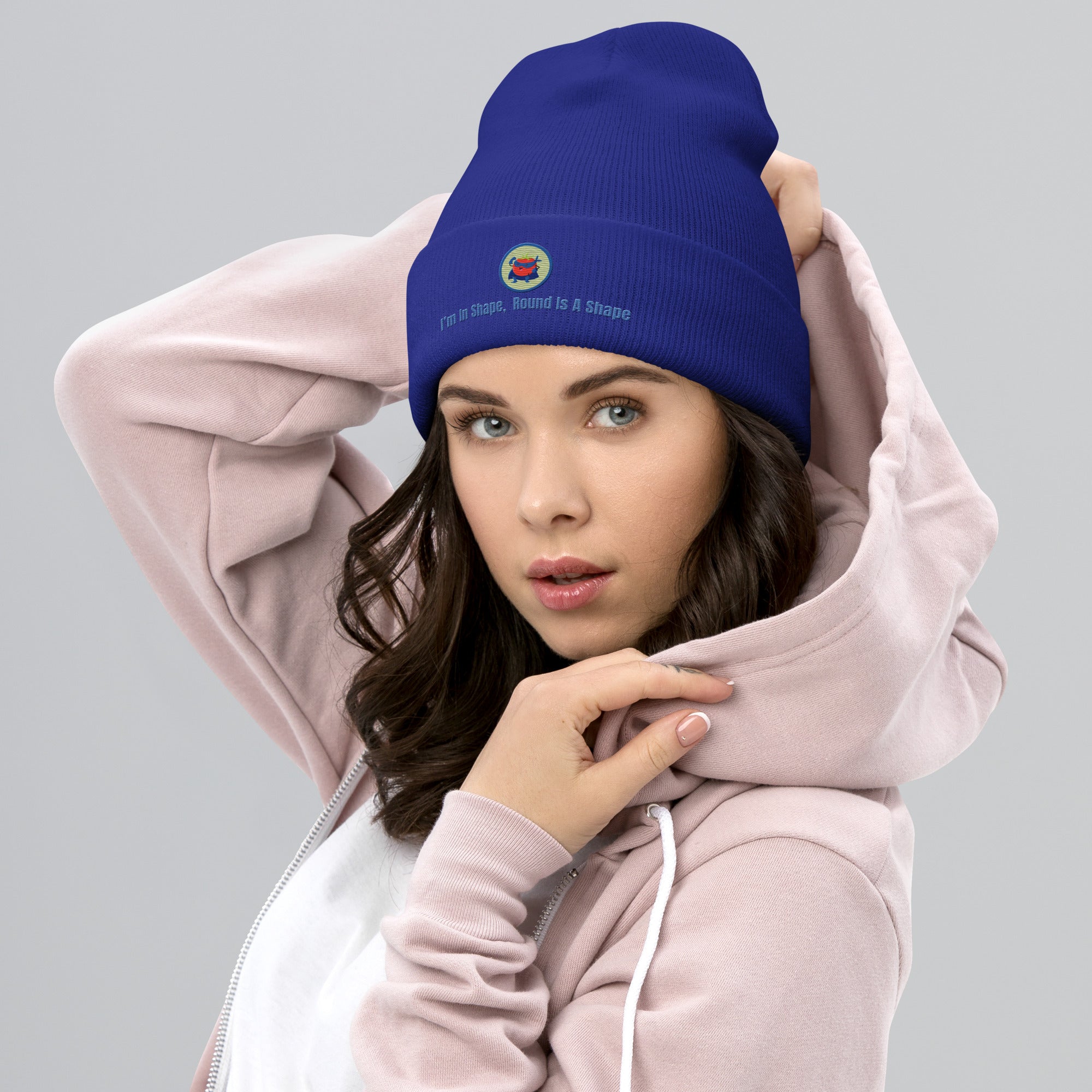 Ein weibliches Model trägt ein Royal Blaues Cuffed Beanie mit einem aufgesticktem Patch eines Tomaten Superhleden (Cartoon) in einem Runden blau-salbeigrünem Rahmen sowie einen schlichten Schriftzug darunter der lautet: "I´m in Shape, Round is A Shape!" auf der Vorderseite. Designed, by Just a Girl.