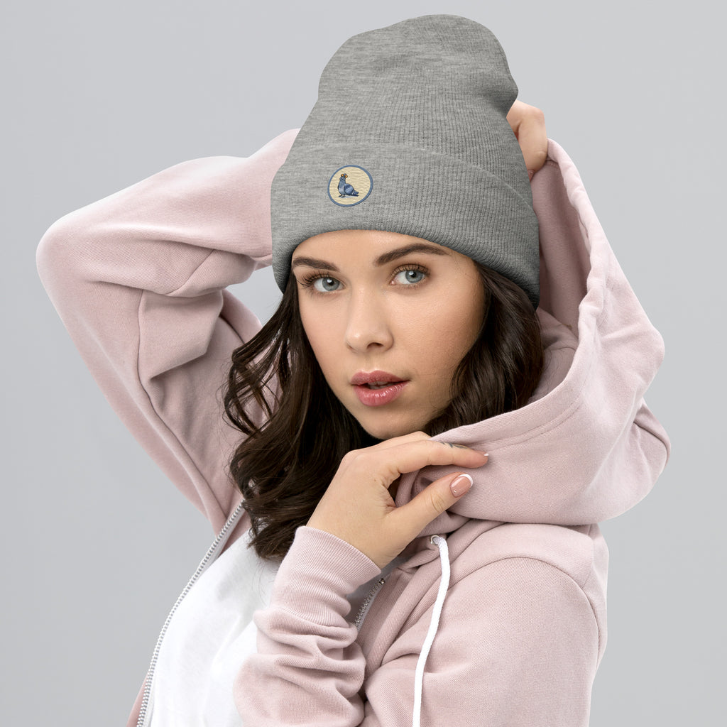 Das weibliche Model trägt eine Heather graue Cuffed Beanie mit aufgestckter Taube in einem grau-beigen rundem Rahmen auf der Vorderseite. Designed, by Just a Girl.
