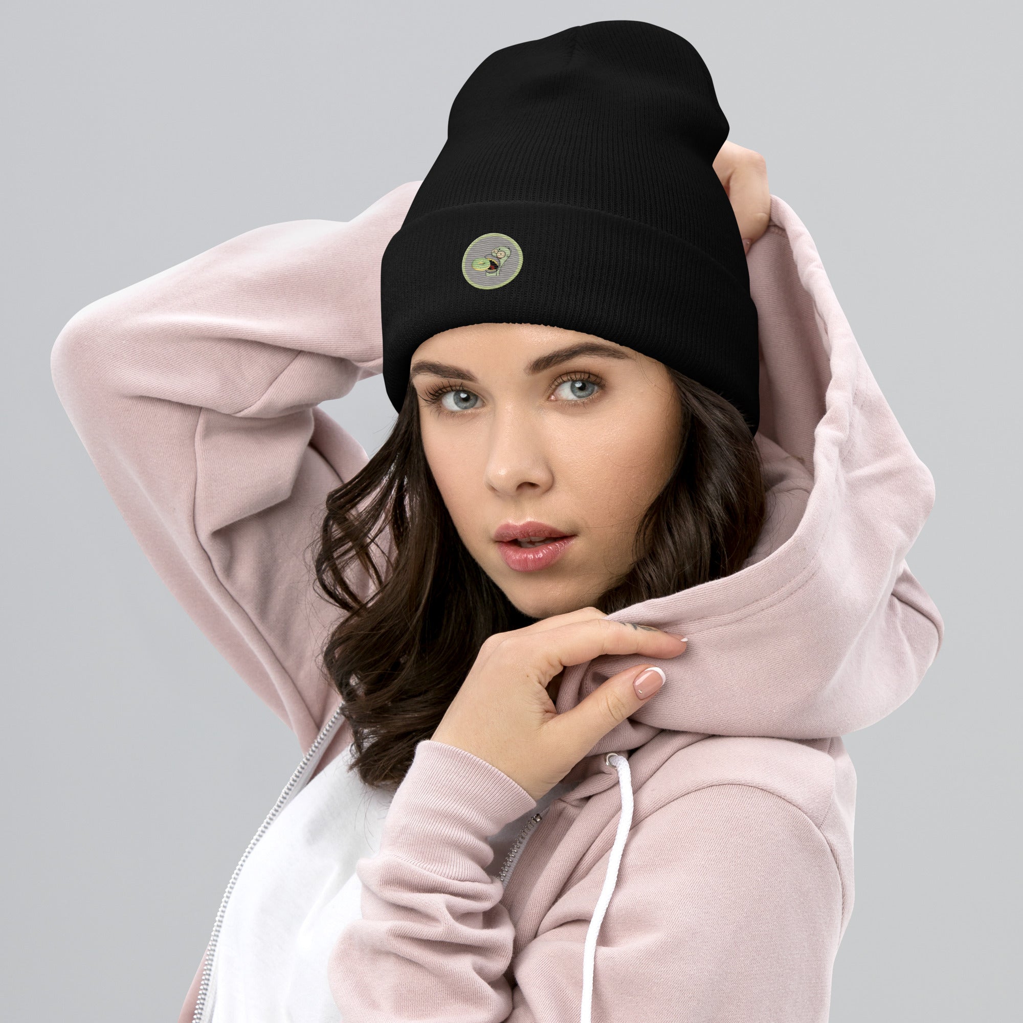 Ein weibliches Model trägt ein schwarzes Cuffed Beanie mit aufgesticktem-homer-monster-gesicht-und einem donut in einem hellgrauen-salbeigrünem Rahmen auf der Vorderseite. Designed, by Just a Girl.