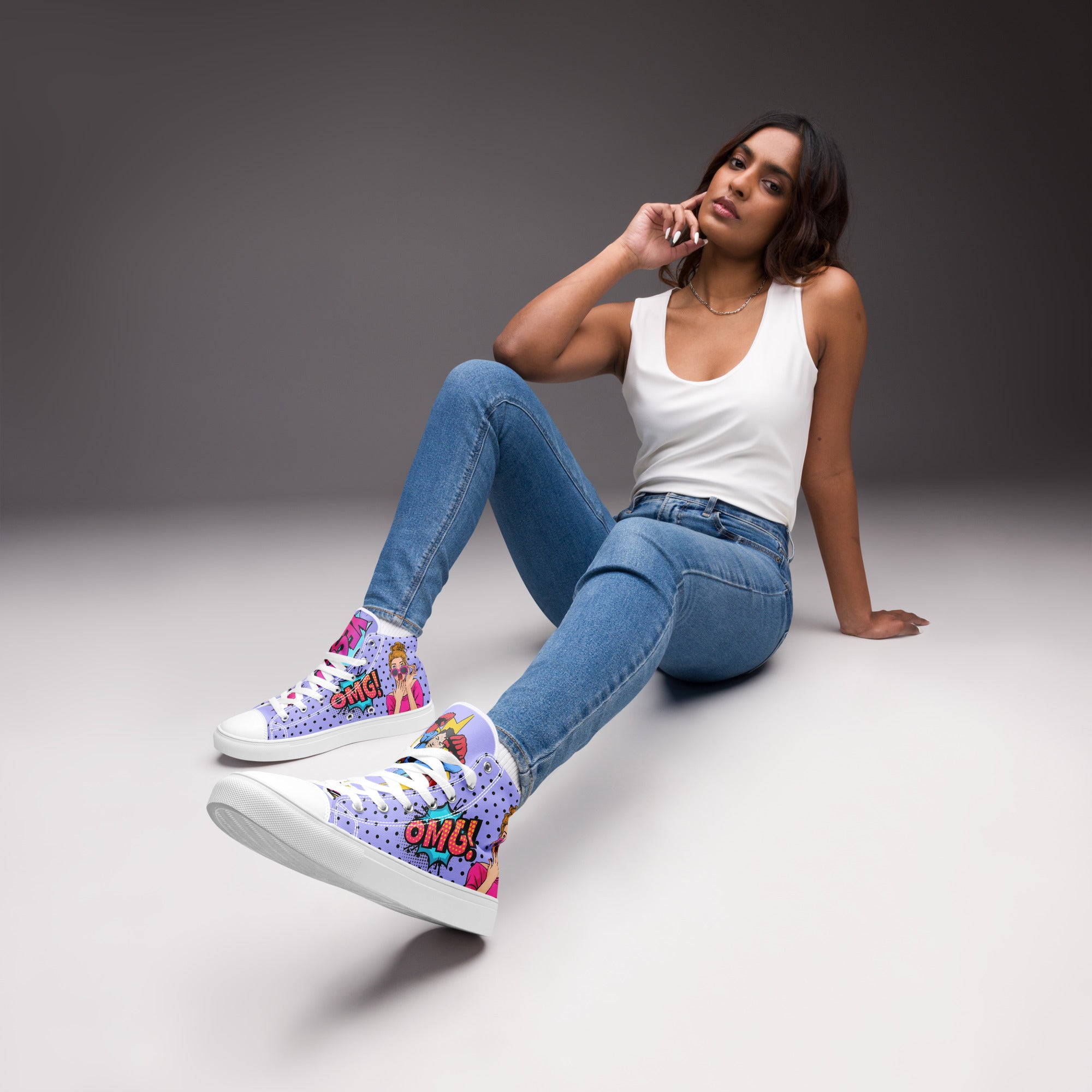 Ein weibliches Model trägt die High-Top-Canvas-Sneaker im Pop-Art-Stil. Der Schuh hat einen lila Hintergrund mit schwarzen Punkten, eine Comic-Frau und eine "OMG!"-Sprechblase. Die linke Schuhzunge zeigt ein Superman-Logo und eine "OK!"-Sprechblase, die rechte Zunge eine "Yesss!"-Sprechblase. Sohlen, Zehenkappen und Schnürsenkel sind weiß. Designed, by Just a Girl.