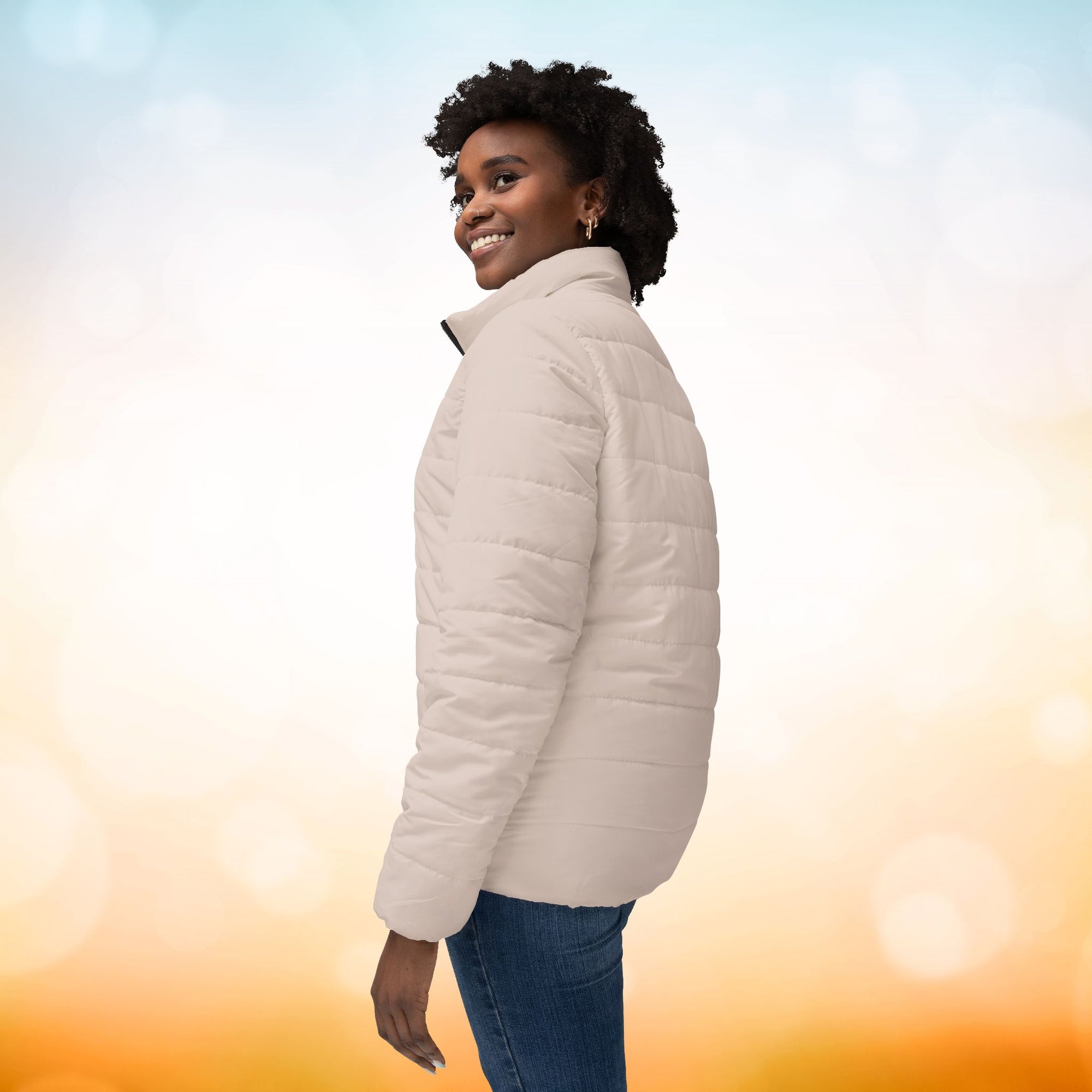 Das weibliche Model zeigt sich der lingen seiten Ansicht mit der  Damen-Pufferjacke in einem zarten Champagner-Rosa. Die Jacke ist horizontal gesteppt, hat eine glatte Oberfläche sowie einen hohen Stehkragen. Designed, by Just a Girl.