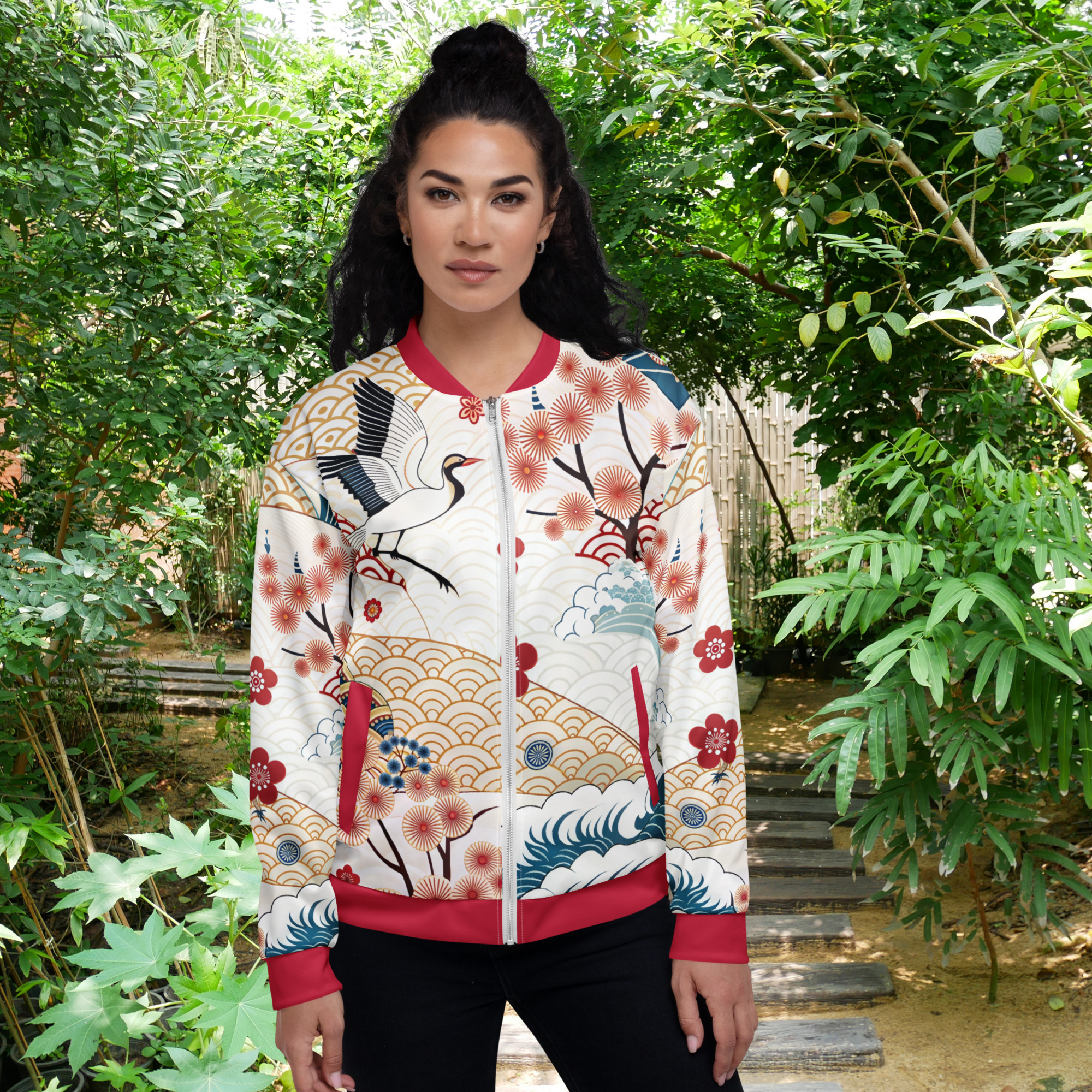 weibliches Model steht mit vorderansicht in einem Gartenumfeld und trägt eine kunstvoll designte Jacke mit japanischen inspiriertem Muster. Die Jacke zeigt florale Kirschblüten, stilisierte Wellen, goldene Fächer Elemente und einen Kranich auBeigen Wellen Hintergrund mit roten Akzenten an Kragen, Bündchen und Taschen. By Just a Girl.