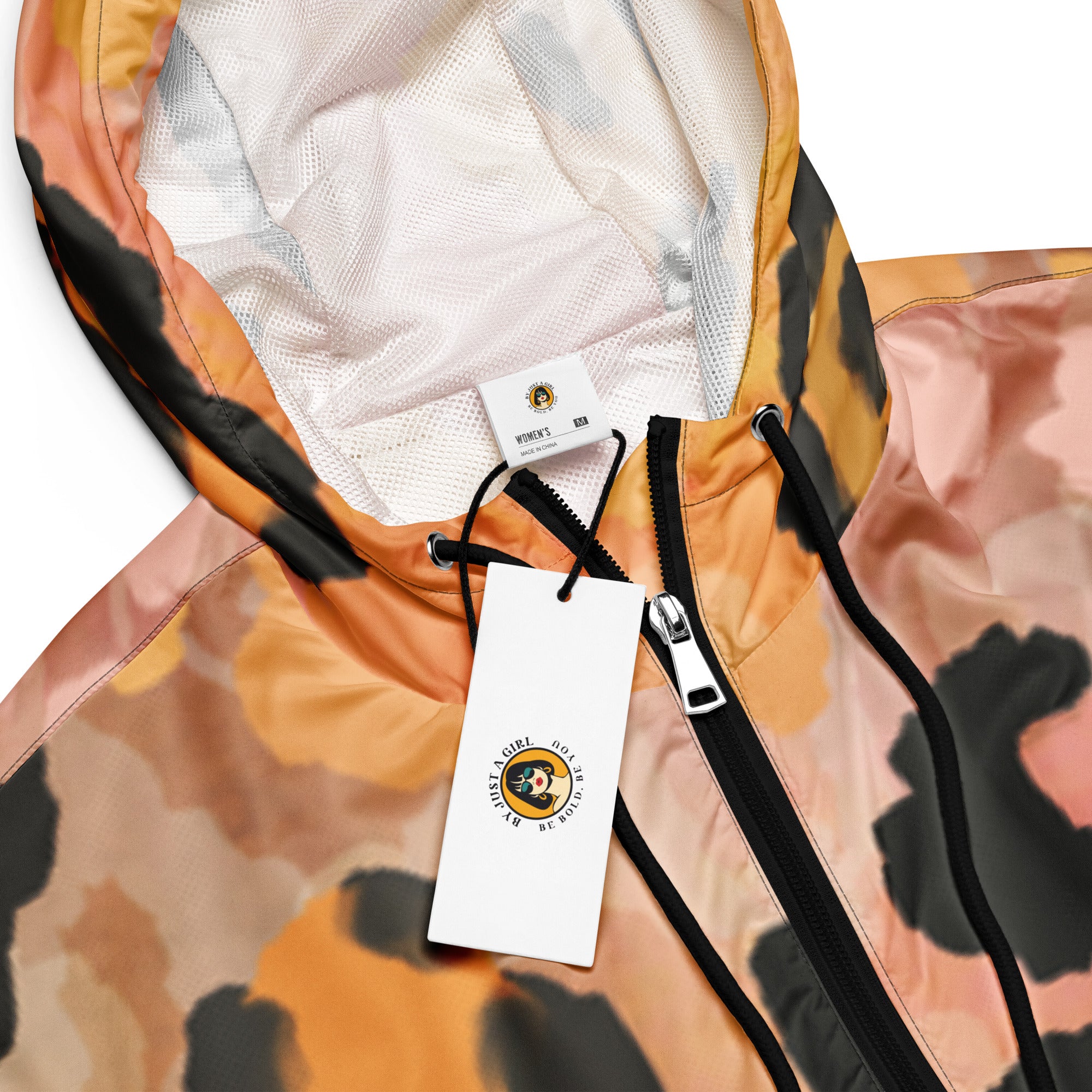 Ein Damen Cropped Windbreaker mit einem abstrakten Leopardenmuster in Orange-, Rosa- und Schwarztönen. Die Jacke hat eine Kapuze, einen halben Reißverschluss mit schwarzen Kordeln und einen verstellbaren Saum. Kapuzenansicht mit Logo. By Just a Girl.