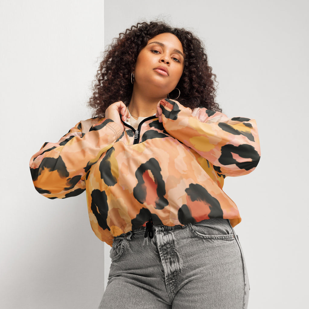 Ein Damen Cropped Windbreaker mit einem abstrakten Leopardenmuster in Orange-, Rosa- und Schwarztönen. Die Jacke hat eine Kapuze, einen halben Reißverschluss mit schwarzen Kordeln und einen verstellbaren Saum. Mockup woman vorderansicht. By Just a Girl.