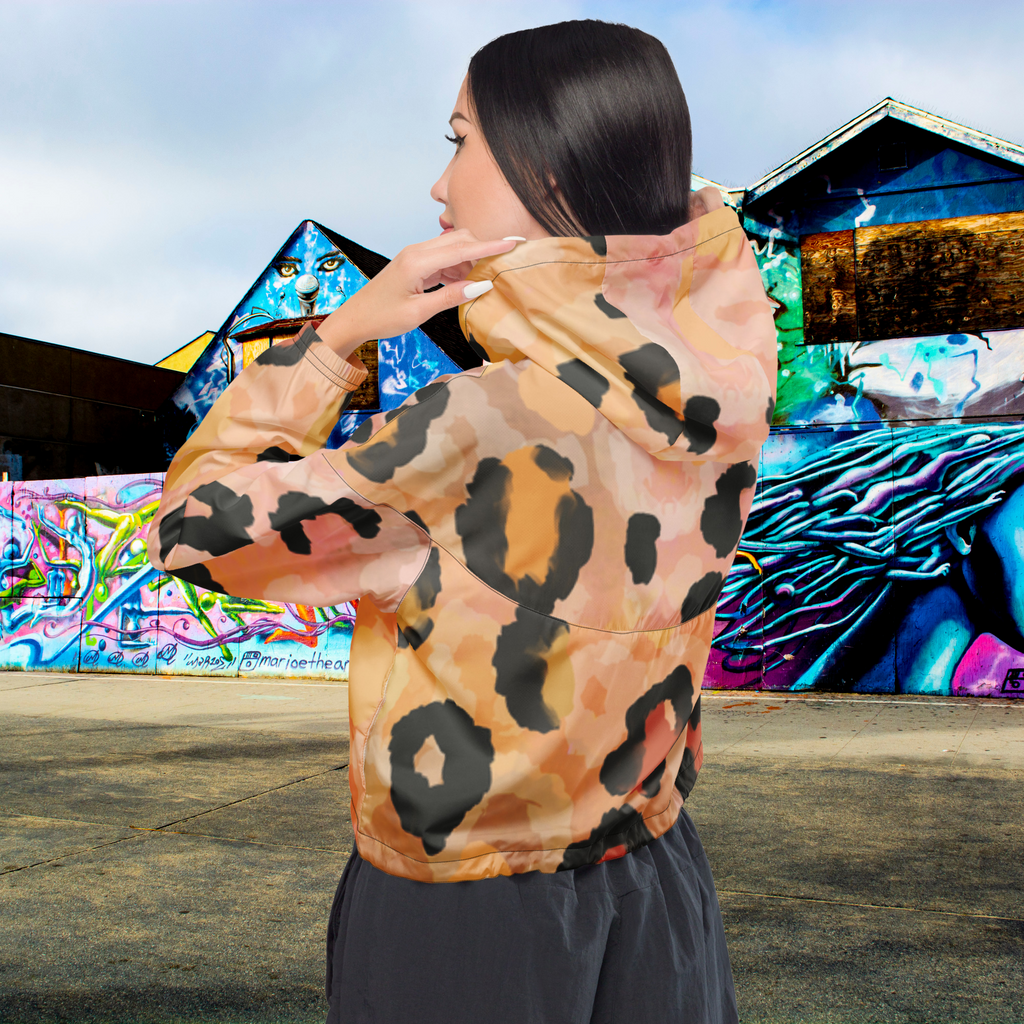 Ein Damen Cropped Windbreaker mit einem abstrakten Leopardenmuster in Orange-, Rosa- und Schwarztönen. Die Jacke hat eine Kapuze, einen halben Reißverschluss mit schwarzen Kordeln und einen verstellbaren Saum. Mockup Girl Rückenansicht. By Just a Girl.