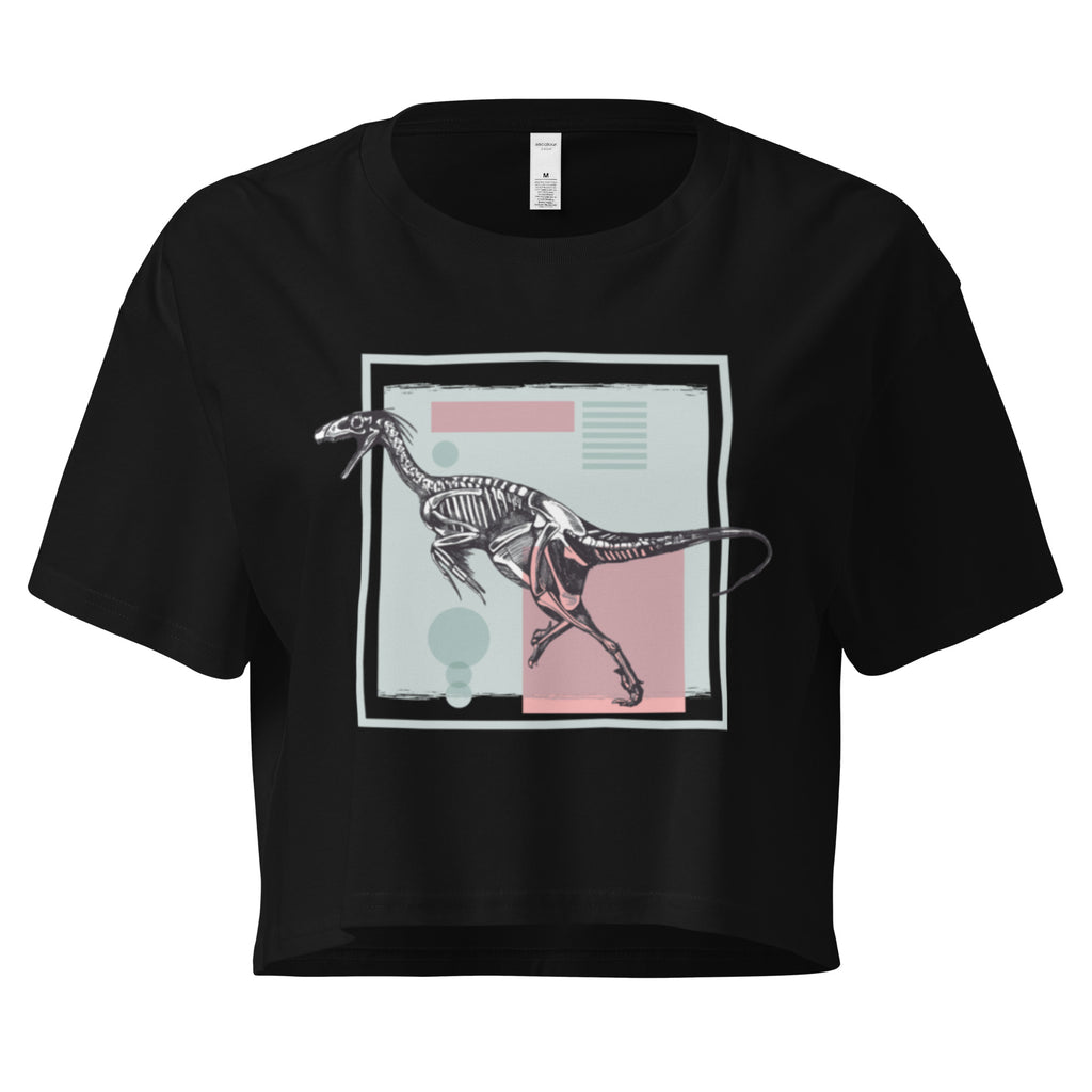Ein schwarzes, kurz geschnittenes Damen-T-Shirt (Crop Top) mit einem weißen Kastenrahmen in der Mitte. Innerhalb des Rahmens befindet sich eine Illustration eines Dinosaurierskeletts, das auf einer Farbfeldfläche aus Rosa und Mintgrün platziert ist. Der Dinosaurier ist in einer Laufhaltung dargestellt.