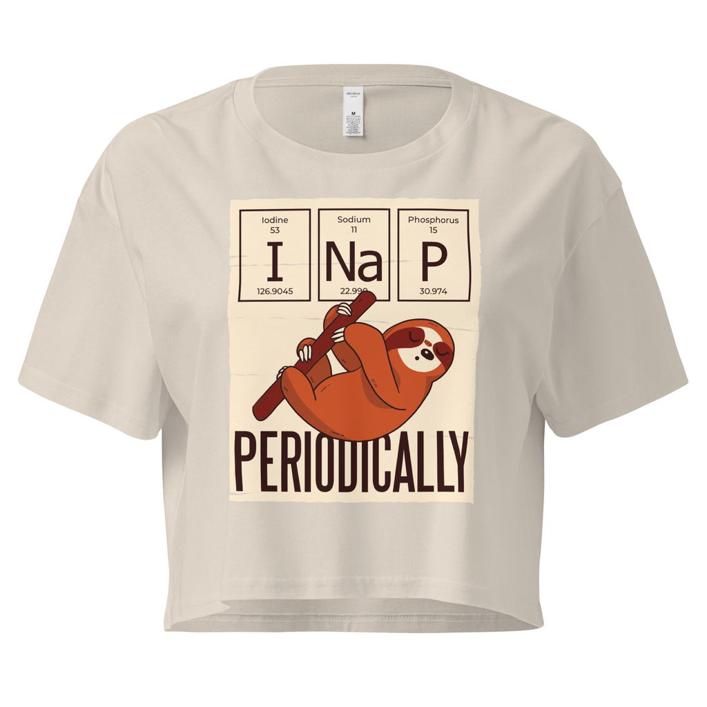 Ein bone oder beige farbenes kurz geschnittenes Damen-T-Shirt (Crop Top) mit einer Illustration eines Faultiers, das an einem Ast hängt. Darüber befinden sich drei Felder im Stil des Periodensystems der Elemente mit den Symbolen "I" (Iodine), "Na" (Sodium) und "P" (Phosphorus), die zusammen "I Na P" bilden. Unter dem Faultier steht das Wort "PERIODICALLY". Der Hintergrund des Motivs ist hellbeige.