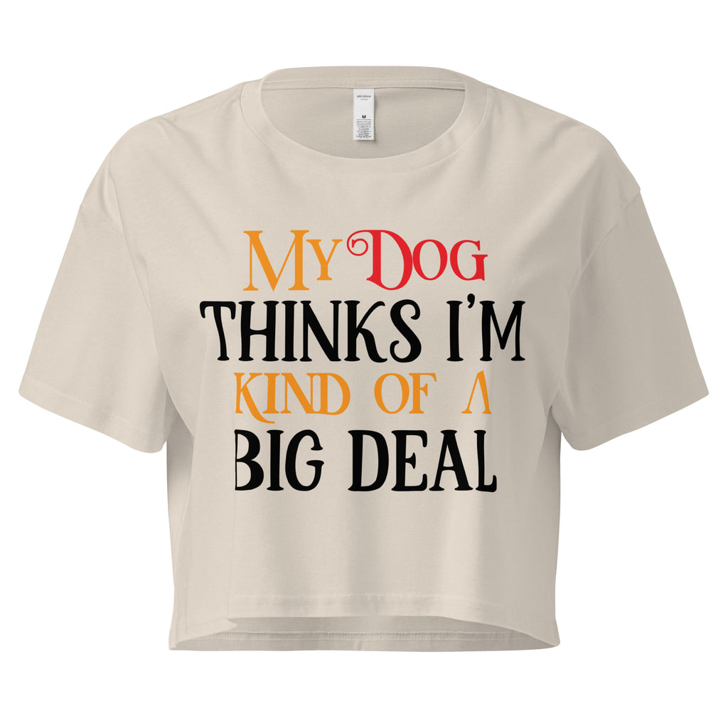 Ein hellbeiges oder cremefarbenes, kurz geschnittenes Damen-T-Shirt (Crop Top) mit dem Text "My Dog THINKS I'M KIND OF A BIG DEAL". Die Wörter "Dog" und "A" sind in Rot, "KIND OF" und "BIG" in Orange, und der restliche Text in Schwarz gehalten.
