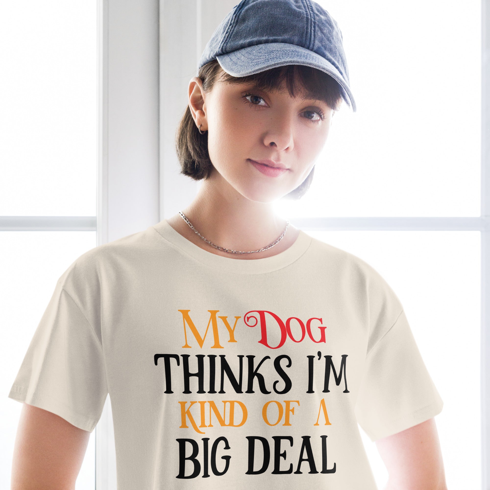 Ein hellbeiges oder cremefarbenes, kurz geschnittenes Damen-T-Shirt (Crop Top) mit dem Text "My Dog THINKS I'M KIND OF A BIG DEAL". Die Wörter "Dog" und "A" sind in Rot, "KIND OF" und "BIG" in Orange, und der restliche Text in Schwarz gehalten.
