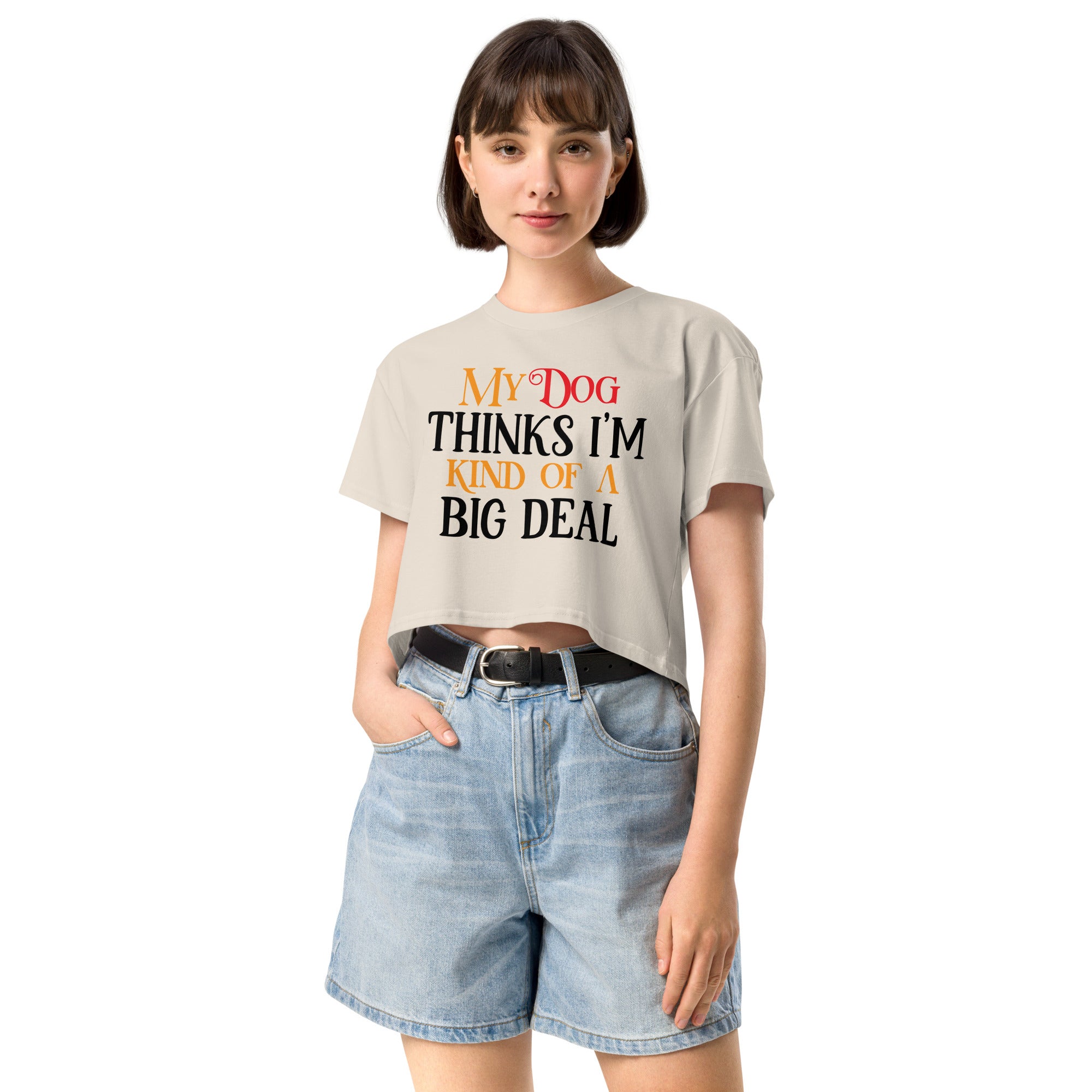 Ein hellbeiges oder cremefarbenes, kurz geschnittenes Damen-T-Shirt (Crop Top) mit dem Text "My Dog THINKS I'M KIND OF A BIG DEAL". Die Wörter "Dog" und "A" sind in Rot, "KIND OF" und "BIG" in Orange, und der restliche Text in Schwarz gehalten.