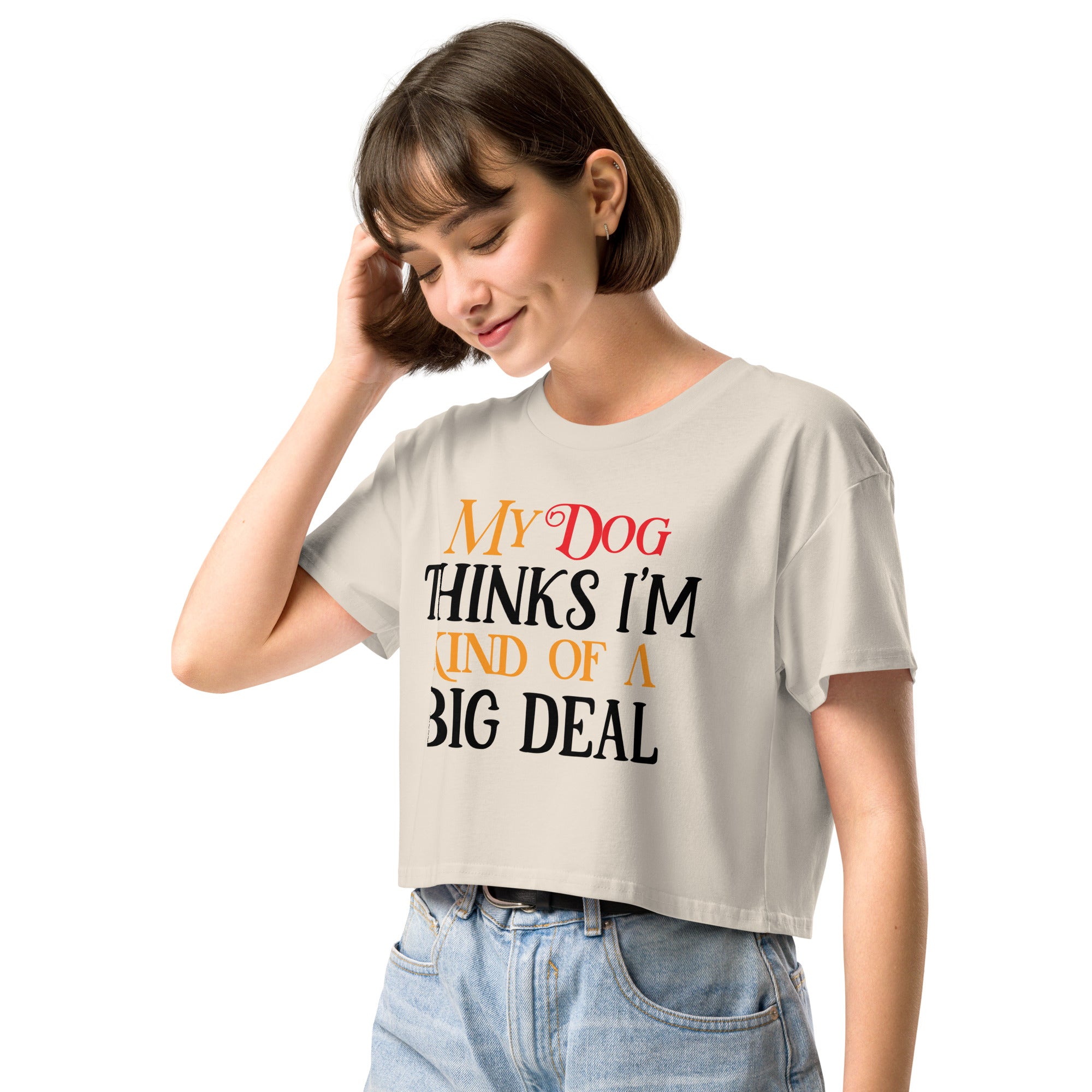 Ein hellbeiges oder cremefarbenes, kurz geschnittenes Damen-T-Shirt (Crop Top) mit dem Text "My Dog THINKS I'M KIND OF A BIG DEAL". Die Wörter "Dog" und "A" sind in Rot, "KIND OF" und "BIG" in Orange, und der restliche Text in Schwarz gehalten.