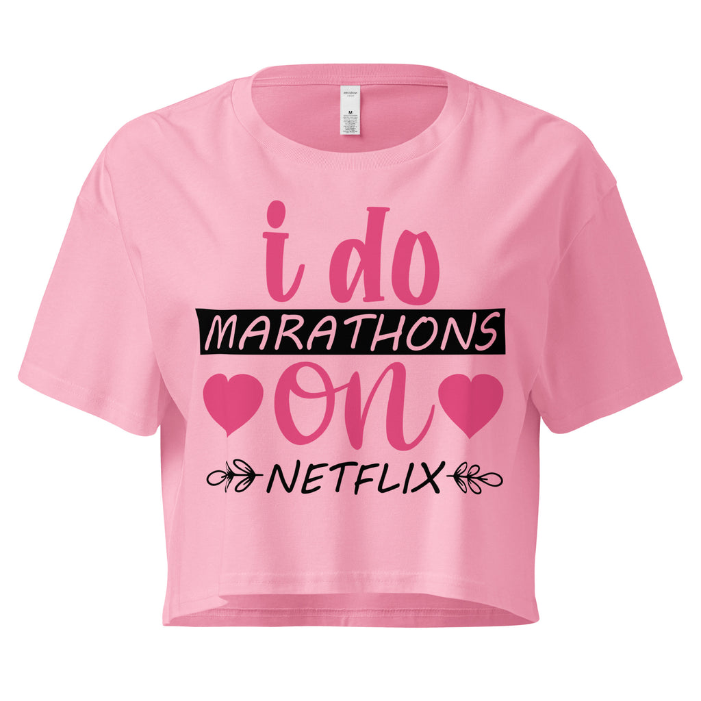 Ein "Bubblegum-Pink" farbenes, kurz geschnittenes Damen-T-Shirt (Crop Top) mit dem Text "i do MARATHONS on NETFLIX" auf der Vorderseite. Der Text "i do" und "on" ist in Pink, "MARATHONS" in Schwarz auf einem schwarzen Balken, und "NETFLIX" ebenfalls in Schwarz, umgeben von kleinen schwarzen Herzen und floralen Ranken.