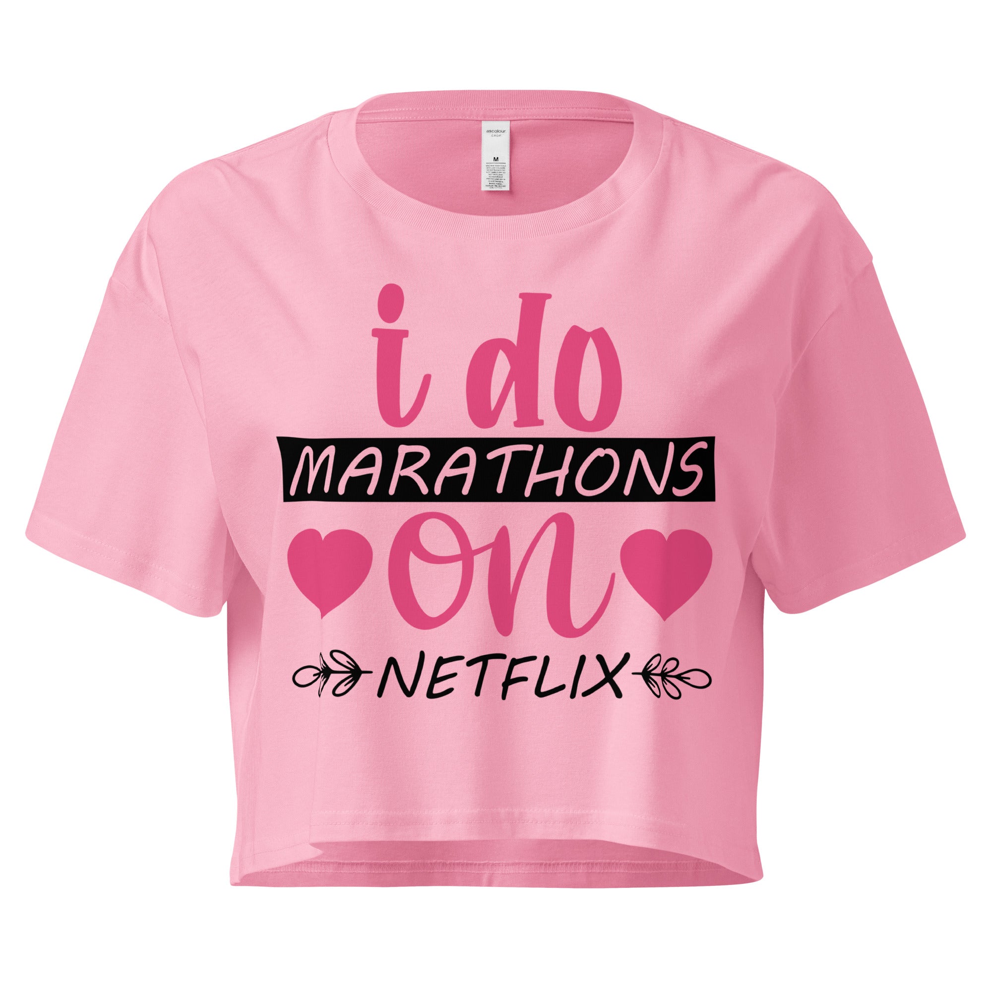 Ein "Bubblegum-Pink" farbenes, kurz geschnittenes Damen-T-Shirt (Crop Top) mit dem Text "i do MARATHONS on NETFLIX" auf der Vorderseite. Der Text "i do" und "on" ist in Pink, "MARATHONS" in Schwarz auf einem schwarzen Balken, und "NETFLIX" ebenfalls in Schwarz, umgeben von kleinen schwarzen Herzen und floralen Ranken.