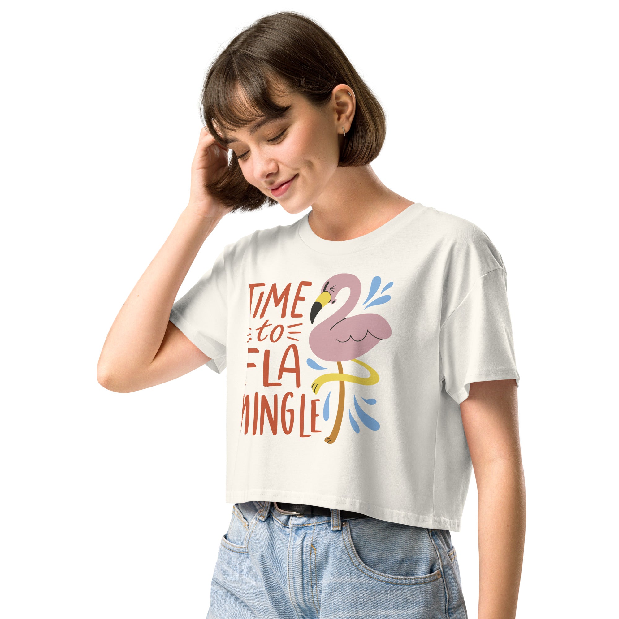 Ein  natur farbenes kurz geschnittenes Damen-T-Shirt (Crop Top) mit einer Illustration eines rosa Flamingos mit gelbem Bein und kleinen blauen Wasserspritzern. Daneben steht der Text "TIME TO FLA MINGLE" in einem verspielten, handgeschriebenen Stil in Orange und Rot.
