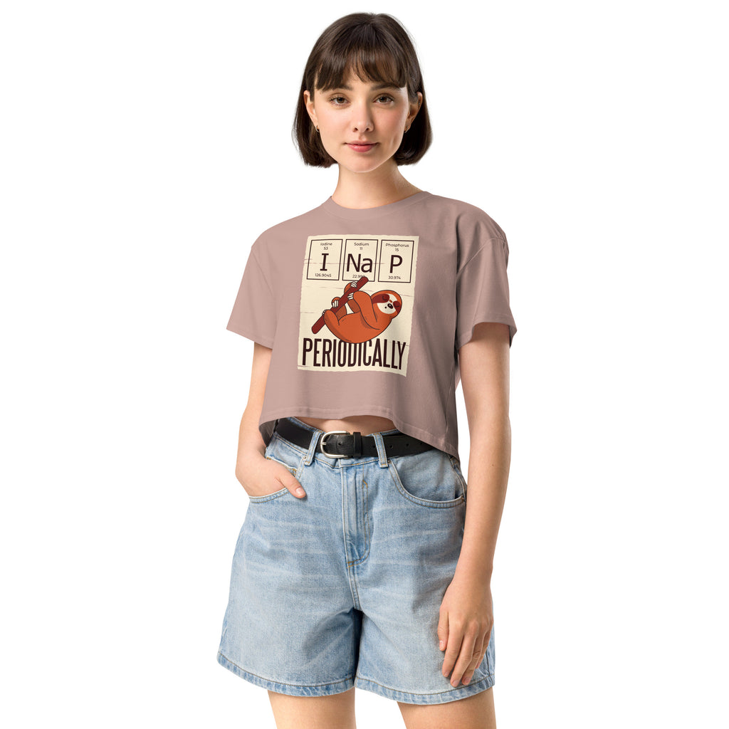 Ein hazy-pink farbenes kurz geschnittenes Damen-T-Shirt (Crop Top) mit einer Illustration eines Faultiers, das an einem Ast hängt. Darüber befinden sich drei Felder im Stil des Periodensystems der Elemente mit den Symbolen "I" (Iodine), "Na" (Sodium) und "P" (Phosphorus), die zusammen "I Na P" bilden. Unter dem Faultier steht das Wort "PERIODICALLY". Der Hintergrund des Motivs ist hellbeige.