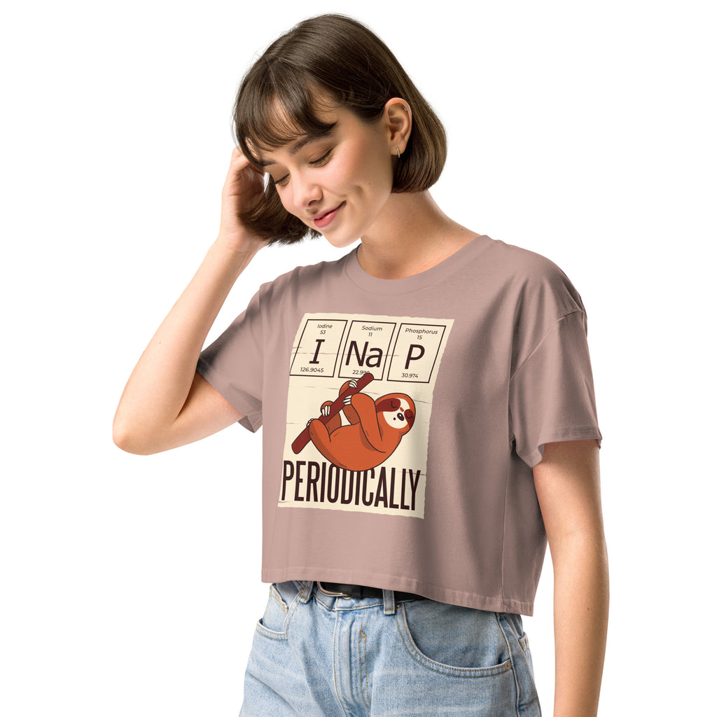 Ein hazy-pink farbenes kurz geschnittenes Damen-T-Shirt (Crop Top) mit einer Illustration eines Faultiers, das an einem Ast hängt. Darüber befinden sich drei Felder im Stil des Periodensystems der Elemente mit den Symbolen "I" (Iodine), "Na" (Sodium) und "P" (Phosphorus), die zusammen "I Na P" bilden. Unter dem Faultier steht das Wort "PERIODICALLY". Der Hintergrund des Motivs ist hellbeige.
