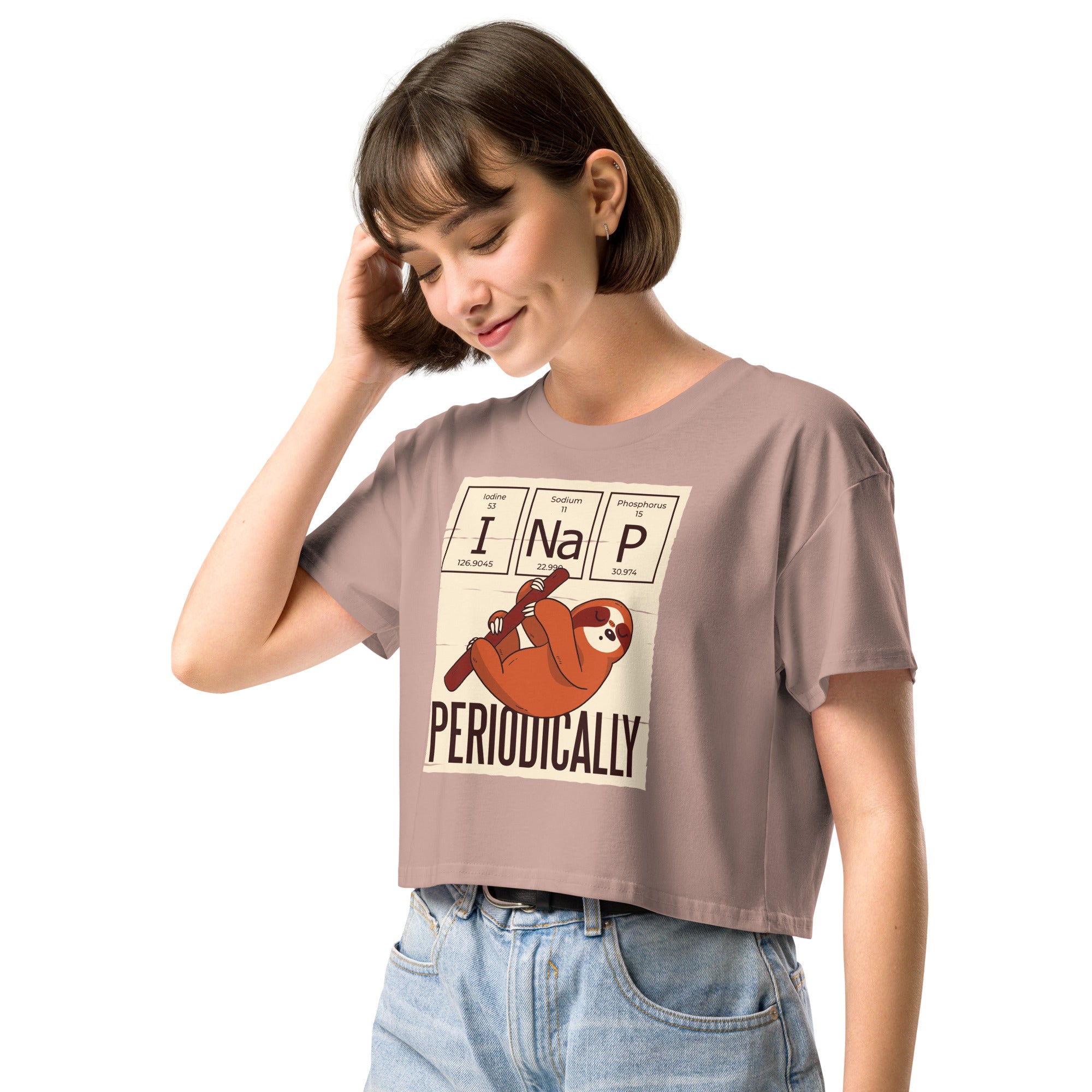 Ein hazy-pink farbenes kurz geschnittenes Damen-T-Shirt (Crop Top) mit einer Illustration eines Faultiers, das an einem Ast hängt. Darüber befinden sich drei Felder im Stil des Periodensystems der Elemente mit den Symbolen "I" (Iodine), "Na" (Sodium) und "P" (Phosphorus), die zusammen "I Na P" bilden. Unter dem Faultier steht das Wort "PERIODICALLY". Der Hintergrund des Motivs ist hellbeige.