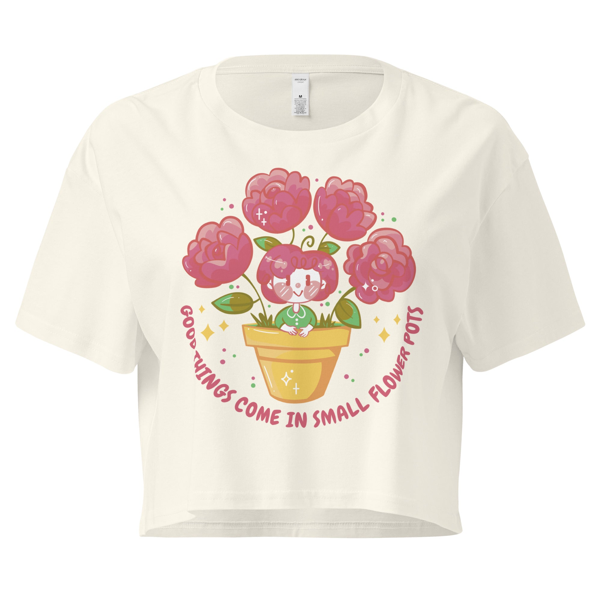 Ein natural farbenes kurz geschnittenes Damen-T-Shirt (Crop Top) mit einer Illustration einer kleinen, lächelnden Figur in einem gelben Blumentopf. Um den Blumentopf herum sind mehrere große, rosa Blüten und grüne Blätter. Der Text "GOOD THINGS COME IN SMALL FLOWER POTS" ist in einem Bogen um das Motiv herum angeordnet, mit kleinen Sternen und Punkten.