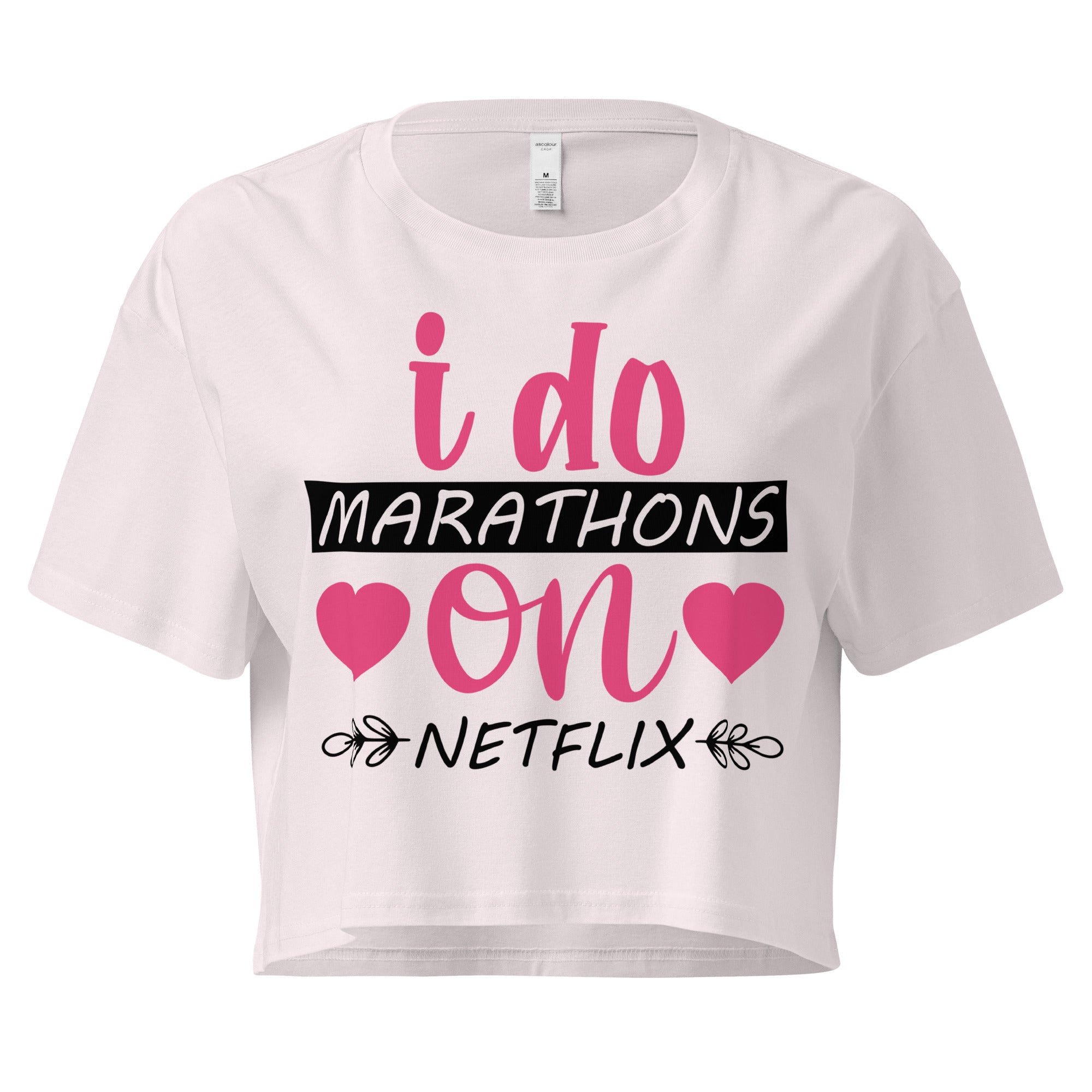Ein orchid farbenes, kurz geschnittenes Damen-T-Shirt (Crop Top) mit dem Text "i do MARATHONS on NETFLIX" auf der Vorderseite. Der Text "i do" und "on" ist in Pink, "MARATHONS" in Schwarz auf einem schwarzen Balken, und "NETFLIX" ebenfalls in Schwarz, umgeben von kleinen schwarzen Herzen und floralen Ranken.