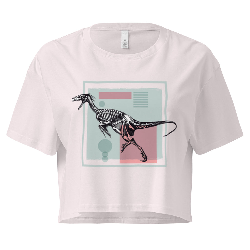 Ein orchid farbenes, kurz geschnittenes Damen-T-Shirt (Crop Top) mit einem weißen Kastenrahmen in der Mitte. Innerhalb des Rahmens befindet sich eine Illustration eines Dinosaurierskeletts, das auf einer Farbfeldfläche aus Rosa und Mintgrün platziert ist. Der Dinosaurier ist in einer Laufhaltung dargestellt.