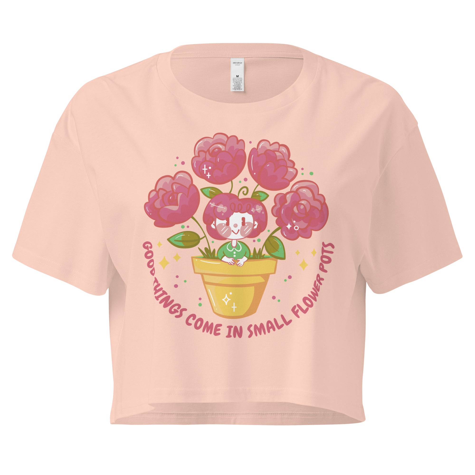 Ein pale-pink farbenes kurz geschnittenes Damen-T-Shirt (Crop Top) mit einer Illustration einer kleinen, lächelnden Figur in einem gelben Blumentopf. Um den Blumentopf herum sind mehrere große, rosa Blüten und grüne Blätter. Der Text "GOOD THINGS COME IN SMALL FLOWER POTS" ist in einem Bogen um das Motiv herum angeordnet, mit kleinen Sternen und Punkten.