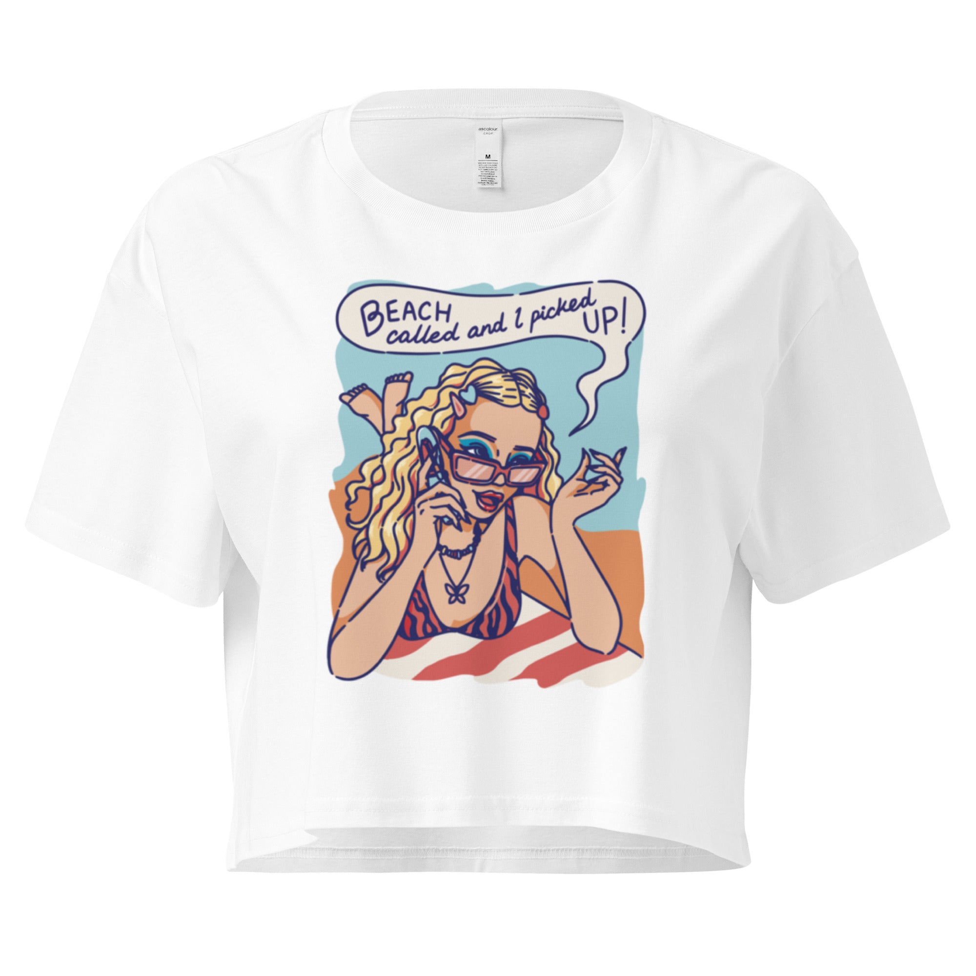 Ein weißes kurz geschnittenes Damen-T-Shirt (Crop Top) mit einer Retro-Illustration einer blonden Frau mit Sonnenbrille und gestreiftem Bikini, die entspannt am Strand liegt und telefoniert. Über ihr ist eine Sprechblase mit dem Text "BEACH called and I picked UP!" zu sehen. Der Hintergrund zeigt Sand und Meer.