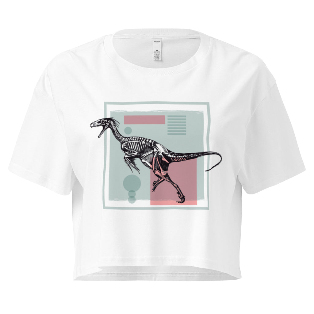 Ein weißes, kurz geschnittenes Damen-T-Shirt (Crop Top) mit einem weißen Kastenrahmen in der Mitte. Innerhalb des Rahmens befindet sich eine Illustration eines Dinosaurierskeletts, das auf einer Farbfeldfläche aus Rosa und Mintgrün platziert ist. Der Dinosaurier ist in einer Laufhaltung dargestellt.