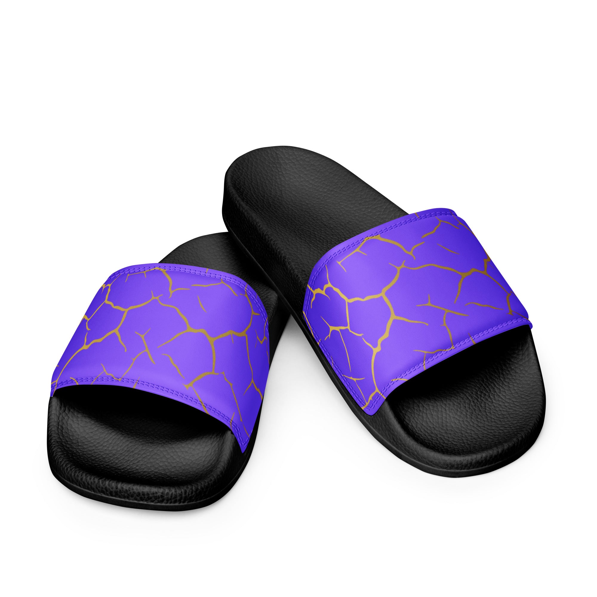 Ein Paar schwarze Flip-Flops mit einem Obermaterial in einem kräftigen Violett, das von einem unregelmäßigen Muster aus gebrochenen goldenen Linien durchzogen ist, die wie Risse oder Sprünge aussehen. Die Riemen sind schwarz und haben eine strukturierte Oberfläche. Auf der Ferse jedes Flip-Flops befindet sich ein rundes gelbes Emblem mit dem Text "BY JUST A GIRL" und "BE BOLD. BE YOU" sowie dem stilisierten Kopf einer Frau mit Bob-Frisur und Sonnenbrille.