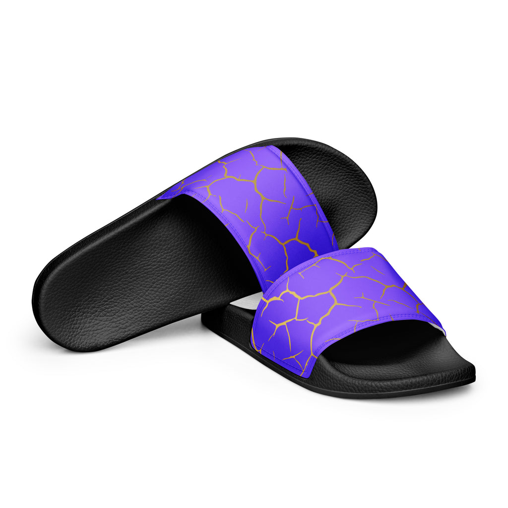 Ein Paar schwarze Flip-Flops mit einem Obermaterial in einem kräftigen Violett, das von einem unregelmäßigen Muster aus gebrochenen goldenen Linien durchzogen ist, die wie Risse oder Sprünge aussehen. Die Riemen sind schwarz und haben eine strukturierte Oberfläche. Auf der Ferse jedes Flip-Flops befindet sich ein rundes gelbes Emblem mit dem Text "BY JUST A GIRL" und "BE BOLD. BE YOU" sowie dem stilisierten Kopf einer Frau mit Bob-Frisur und Sonnenbrille.