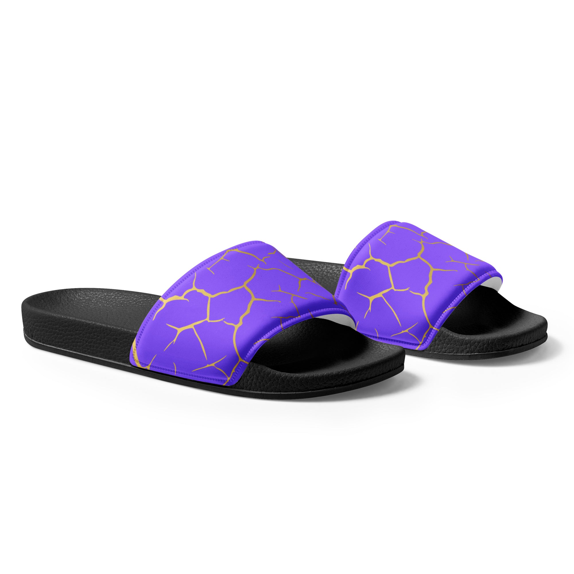 Ein Paar schwarze Flip-Flops mit einem Obermaterial in einem kräftigen Violett, das von einem unregelmäßigen Muster aus gebrochenen goldenen Linien durchzogen ist, die wie Risse oder Sprünge aussehen. Die Riemen sind schwarz und haben eine strukturierte Oberfläche. Auf der Ferse jedes Flip-Flops befindet sich ein rundes gelbes Emblem mit dem Text "BY JUST A GIRL" und "BE BOLD. BE YOU" sowie dem stilisierten Kopf einer Frau mit Bob-Frisur und Sonnenbrille.